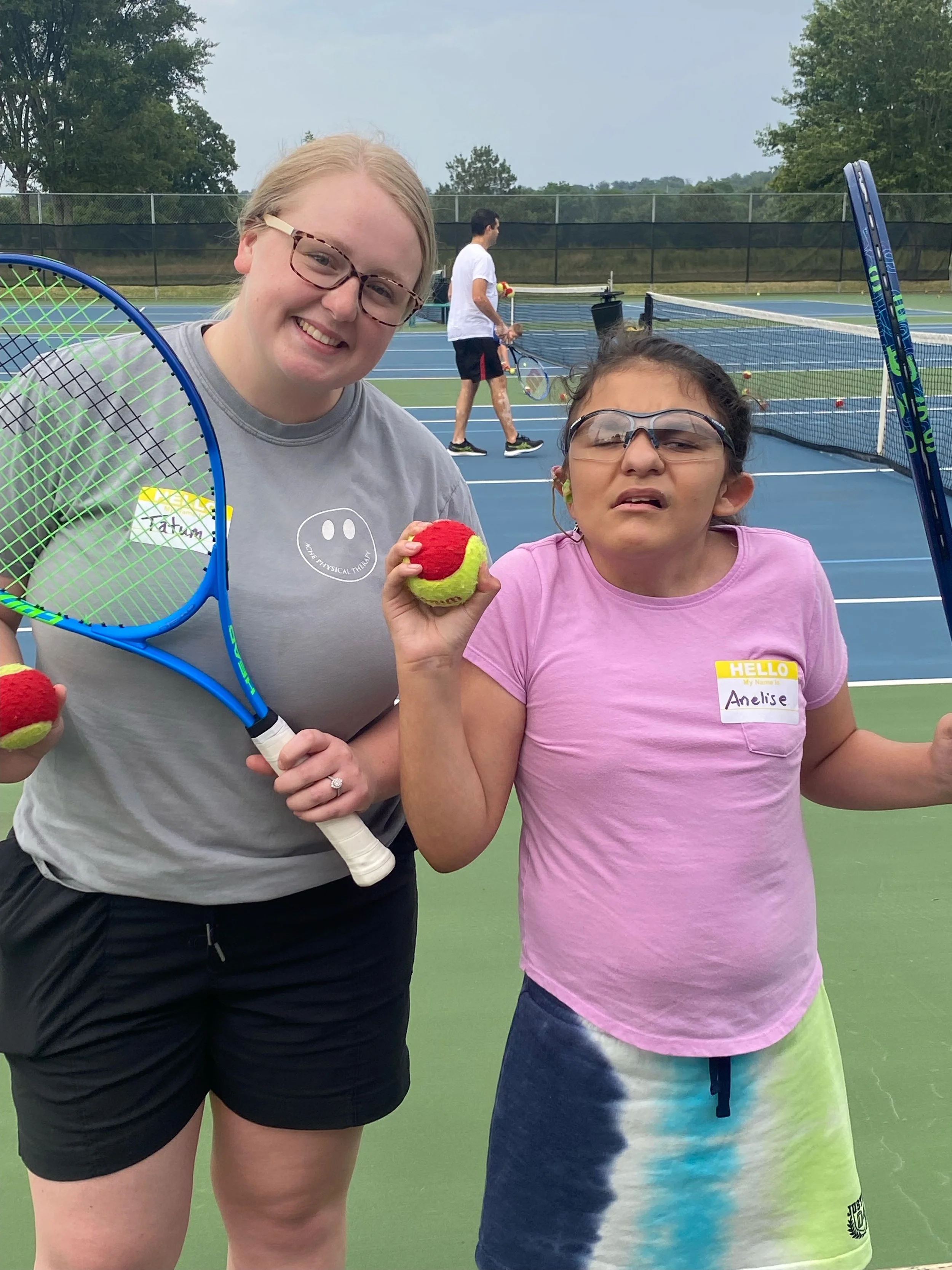 girl & volunteer smiling holding a tennis ball & racquet