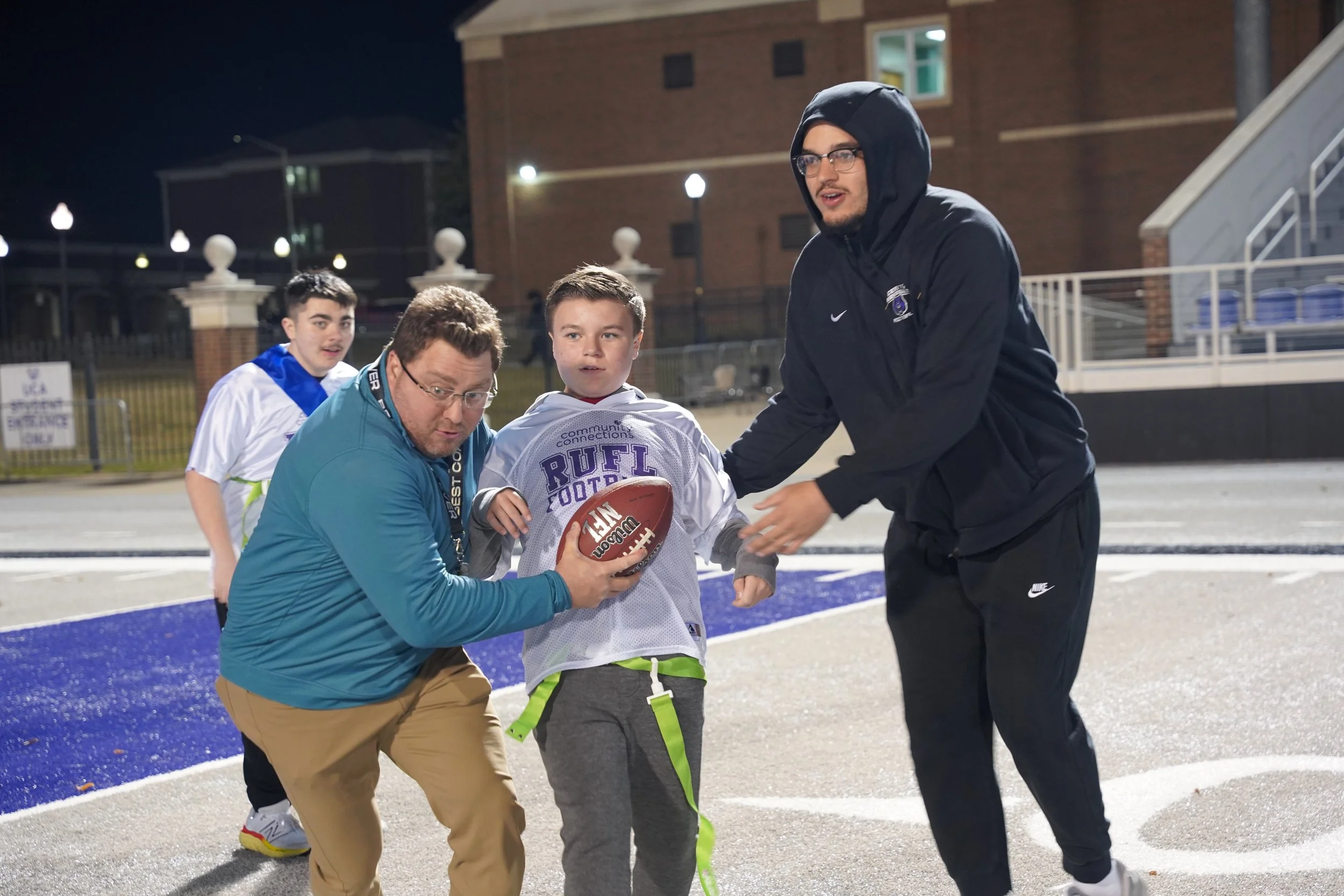 two volunteers helping a boy run with football