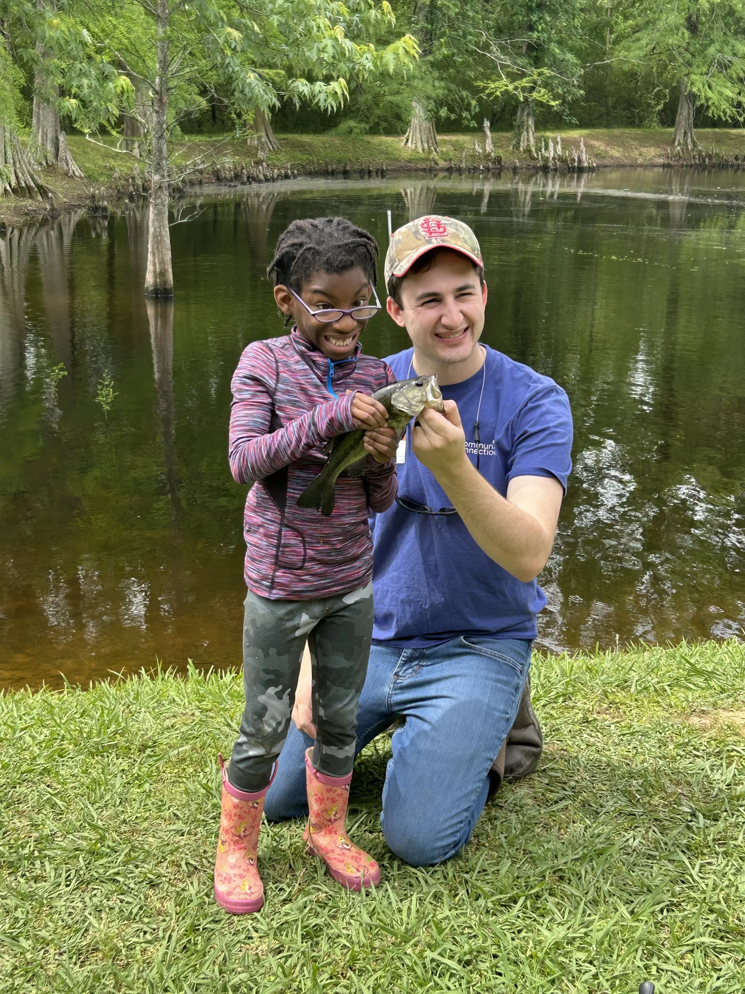 volunteer with girl holding fish by a pond