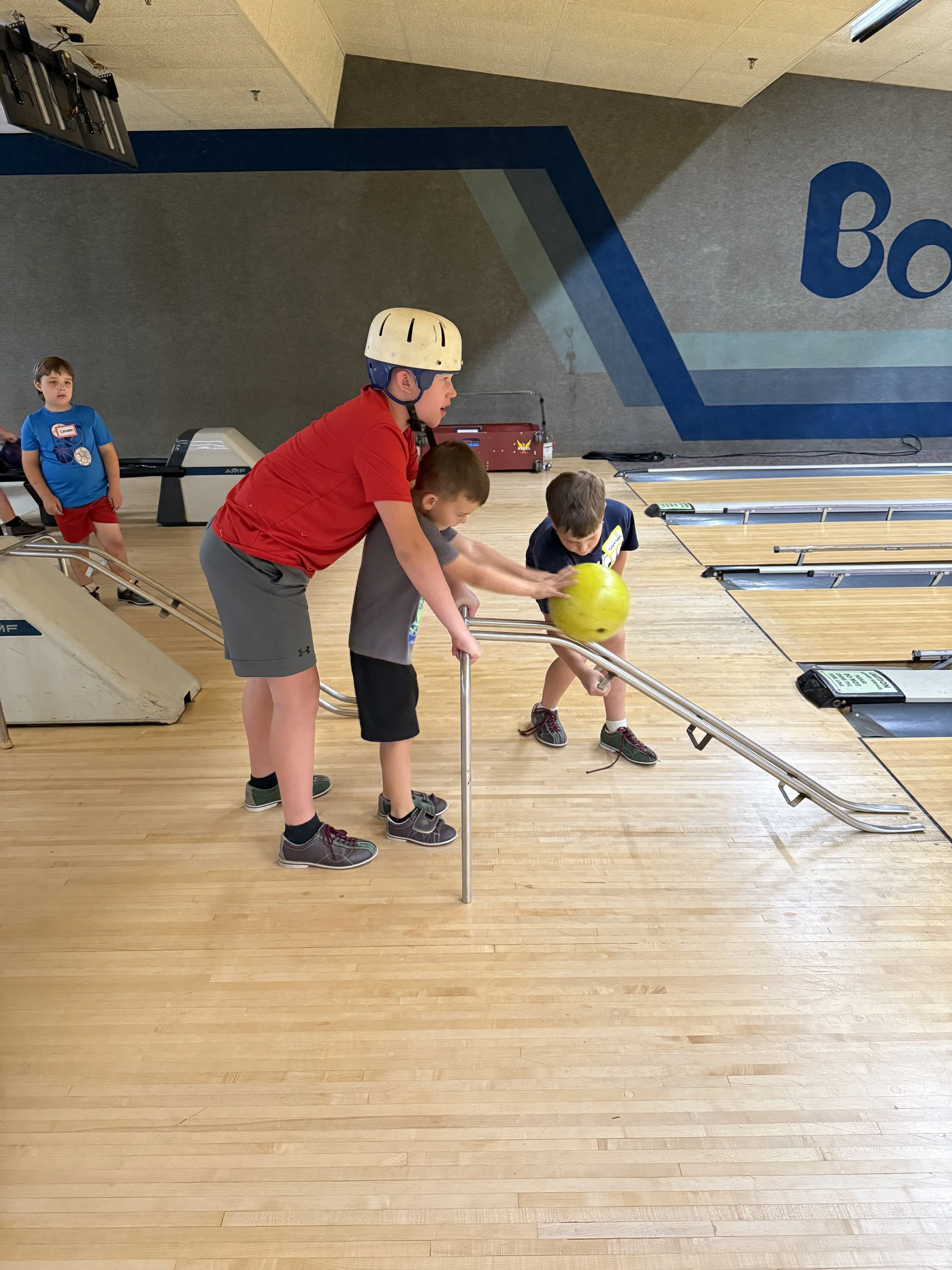 two boys rolling bowling ball using a ramp