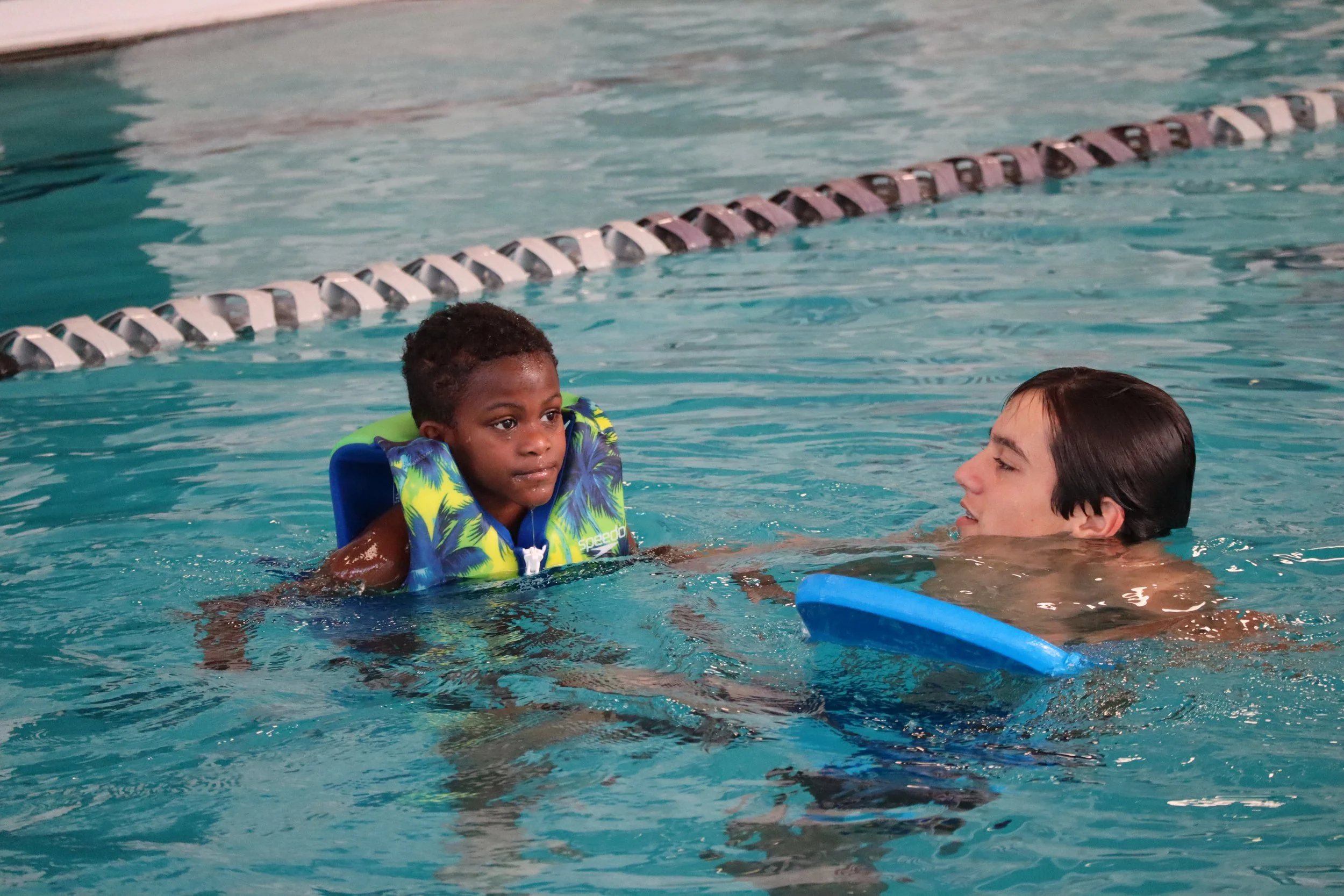 child with life jacket swimming in pool with volunteer