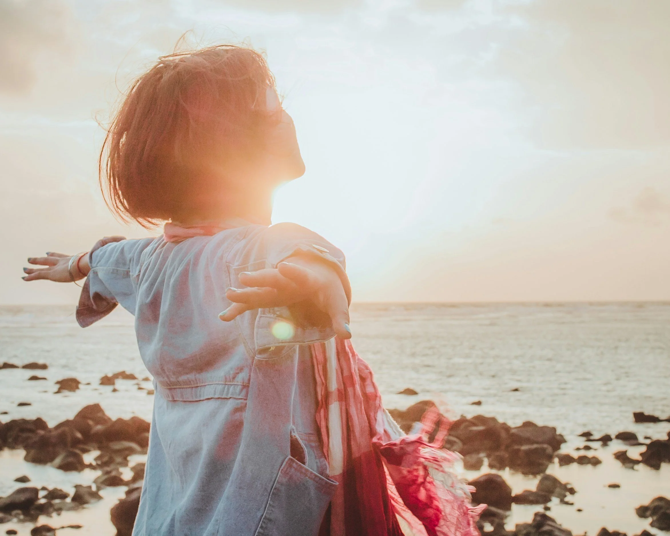 Frau am Strand bei Sonnenuntergang, die die Arme ausbreitet.