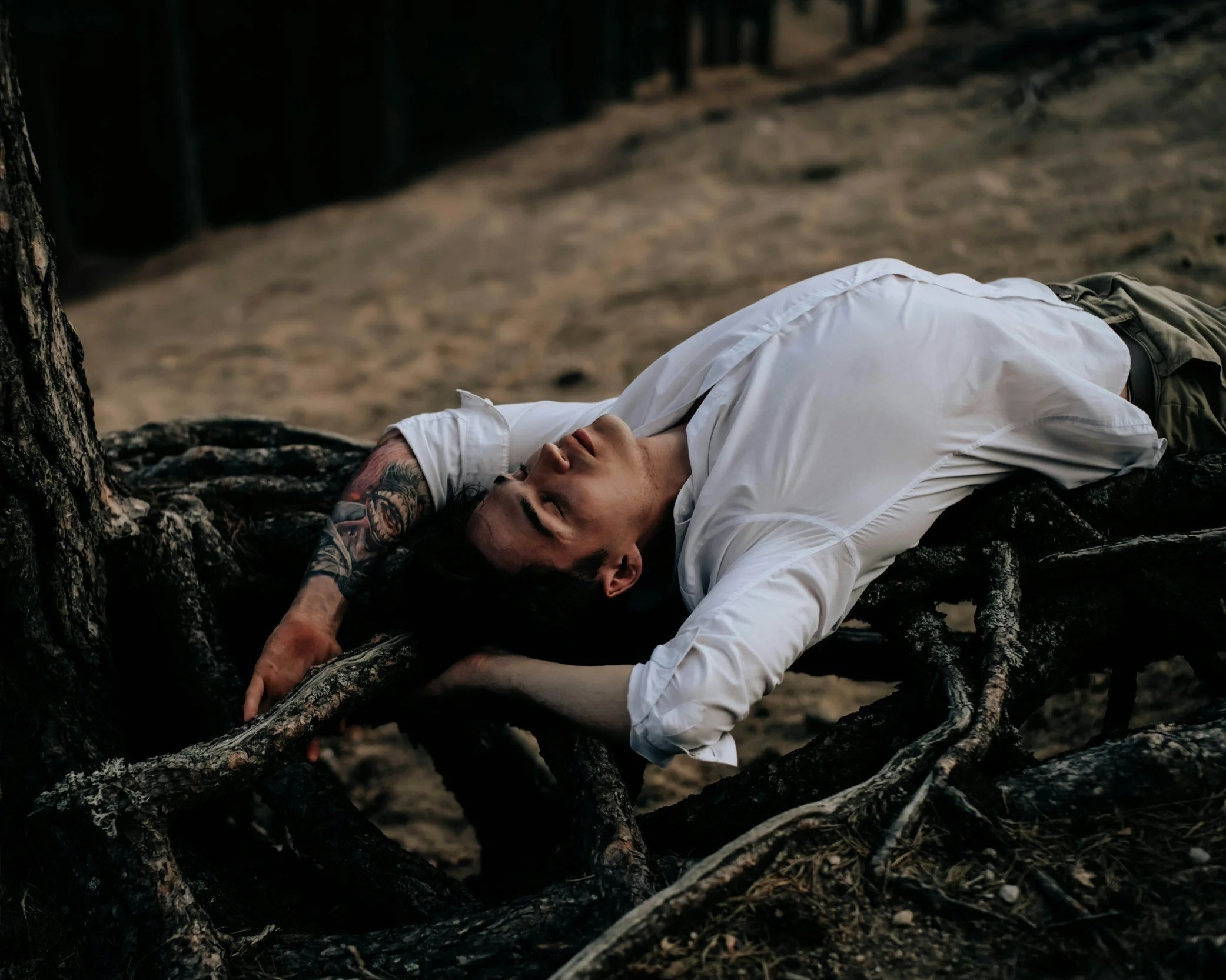 Mann liegt auf verdorrten Ästen, mit geschlossenen Augen und entspanntem Gesicht, im Freien