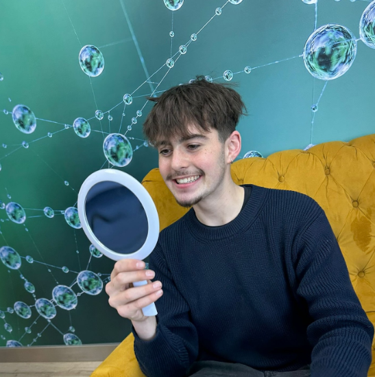 Young male patient smiling while checking his teeth in a handheld mirror at a modern orthodontic clinic in Greystones.