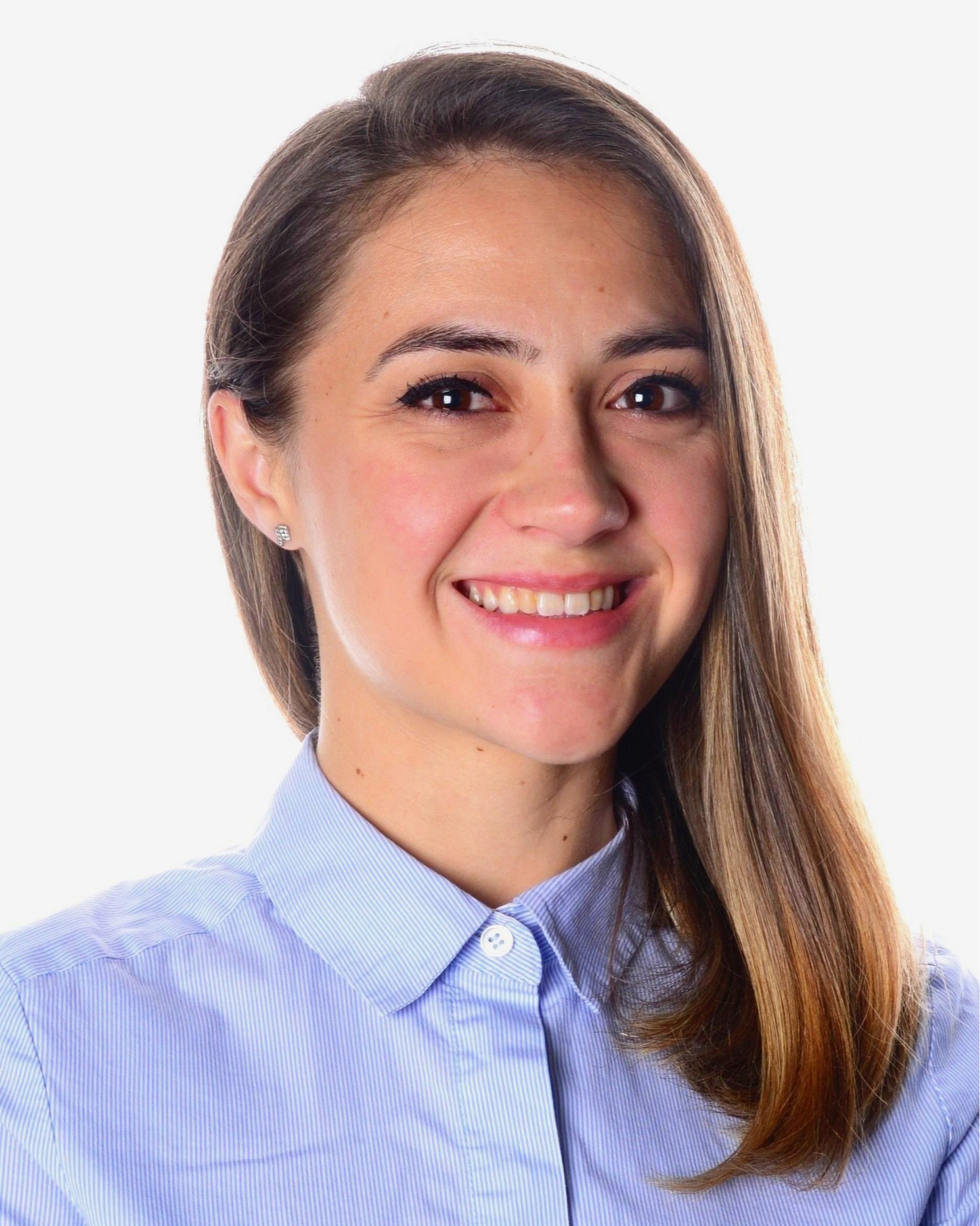 Close-up of a smiling woman with brown hair, wearing a light blue button-up shirt and earrings, against a white background.