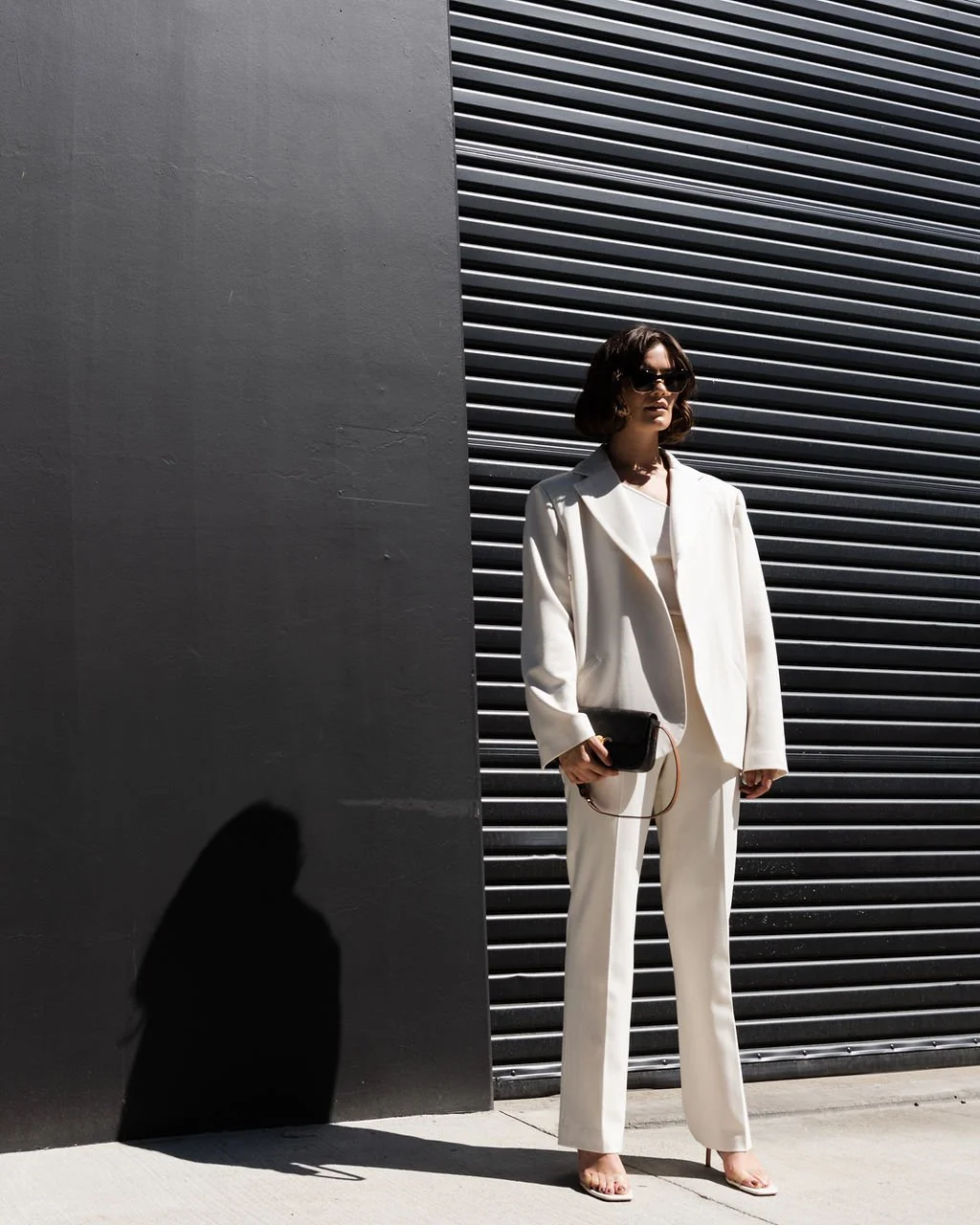 Woman wearing a white suit holding a black clutch. 