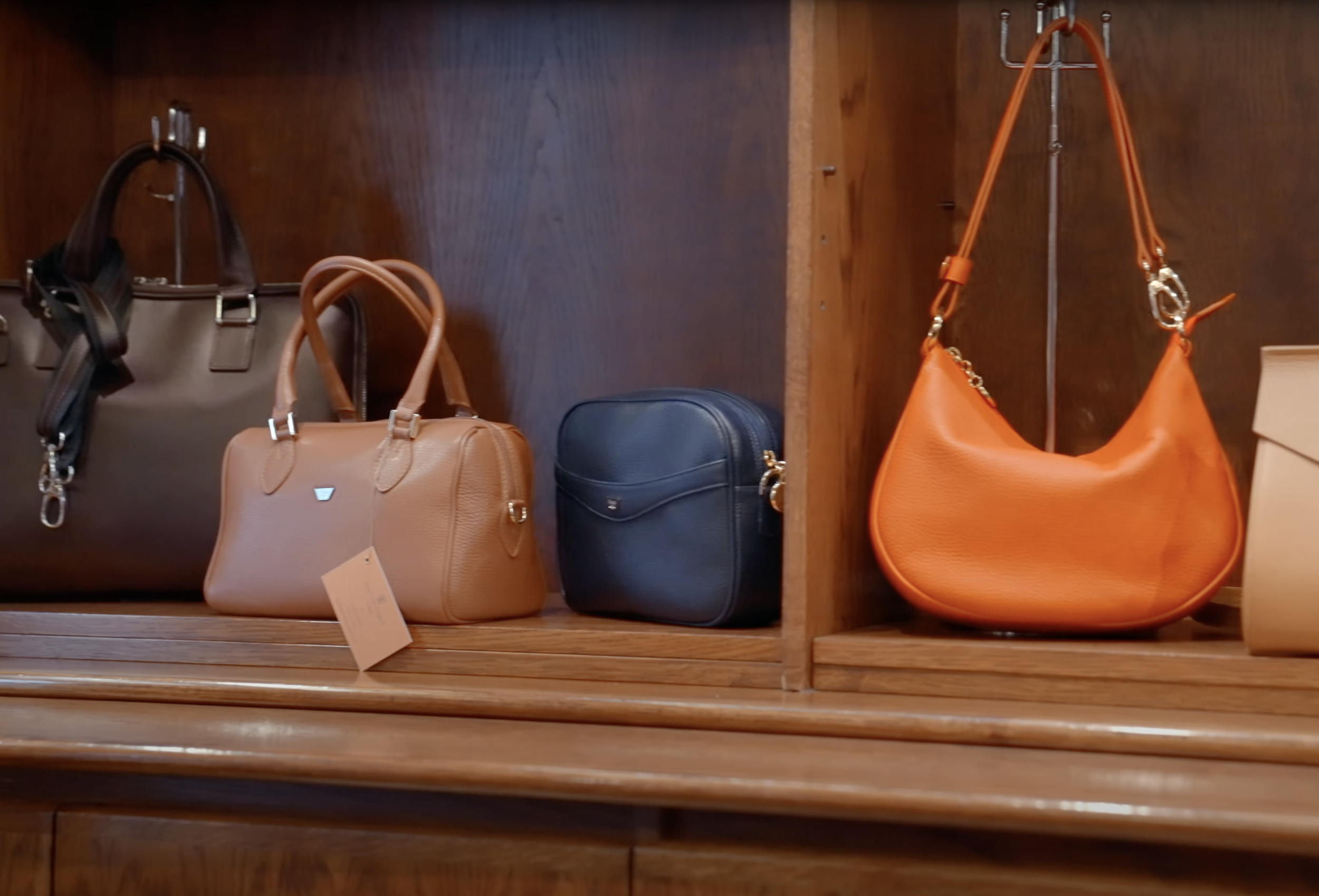 Assortment of leather handbags on wooden shelves, including a brown satchel, tan handbag, blue purse, and orange shoulder bag.