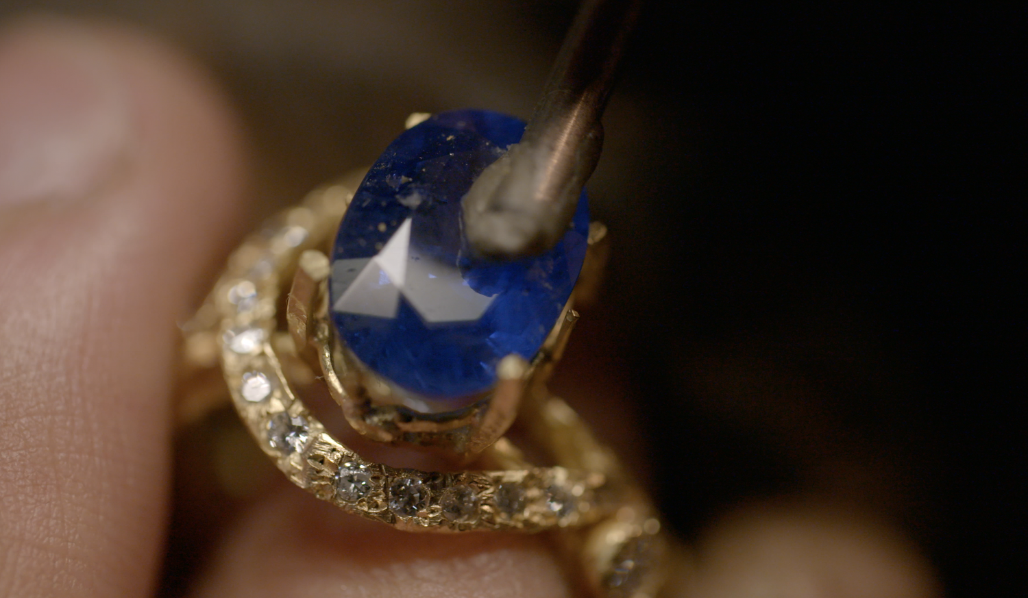 Close-up of a gold ring with a large blue gemstone and smaller diamonds being polished.