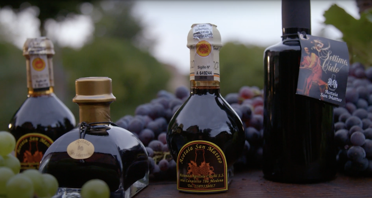Bottles of balsamic vinegar on a table with grapes in the background.