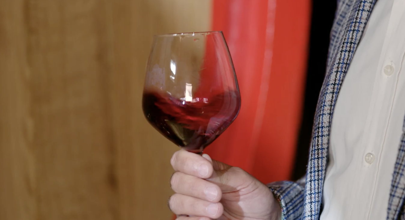 Person holding a glass of red wine with a swirling motion.