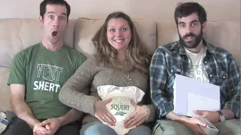 Surprise! Baby on board. 

Image: two dark-haired white men on either side of a blonde white woman; man on left, with a surprised expression, is wearing a green t-shirt reading "YERT SHERT"; the woman is holding a onsie reading "YERT SQUERT" and is s