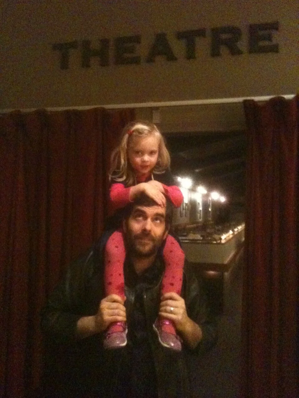 The YERT baby finds a new, sustainable form of transportation. 

Image: small, blond child riding on the shoulders of her father under a sign that reads, "Theatre."