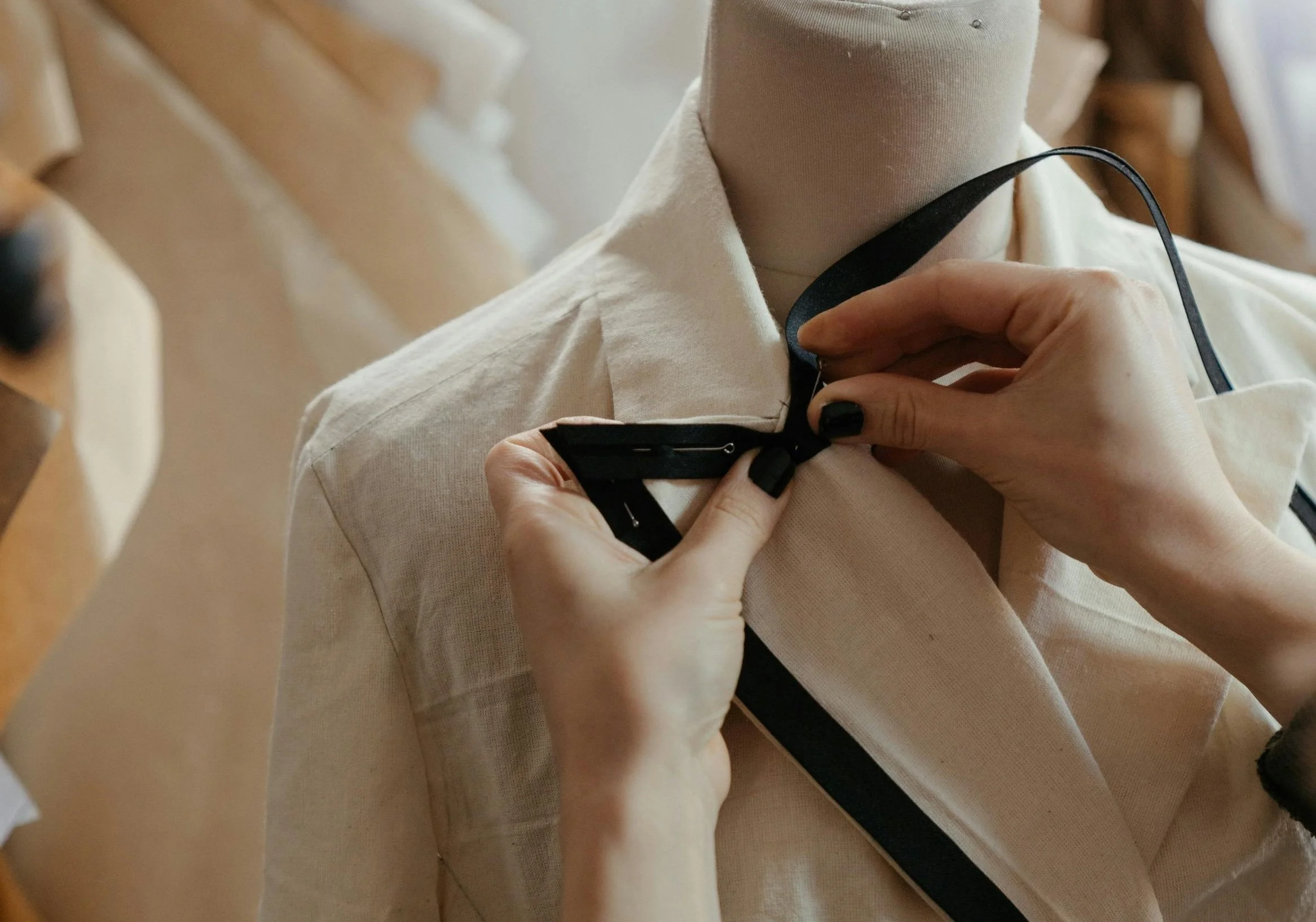 A person is adjusting a black ribbon tie on a mannequin wearing a cream-colored shirt.