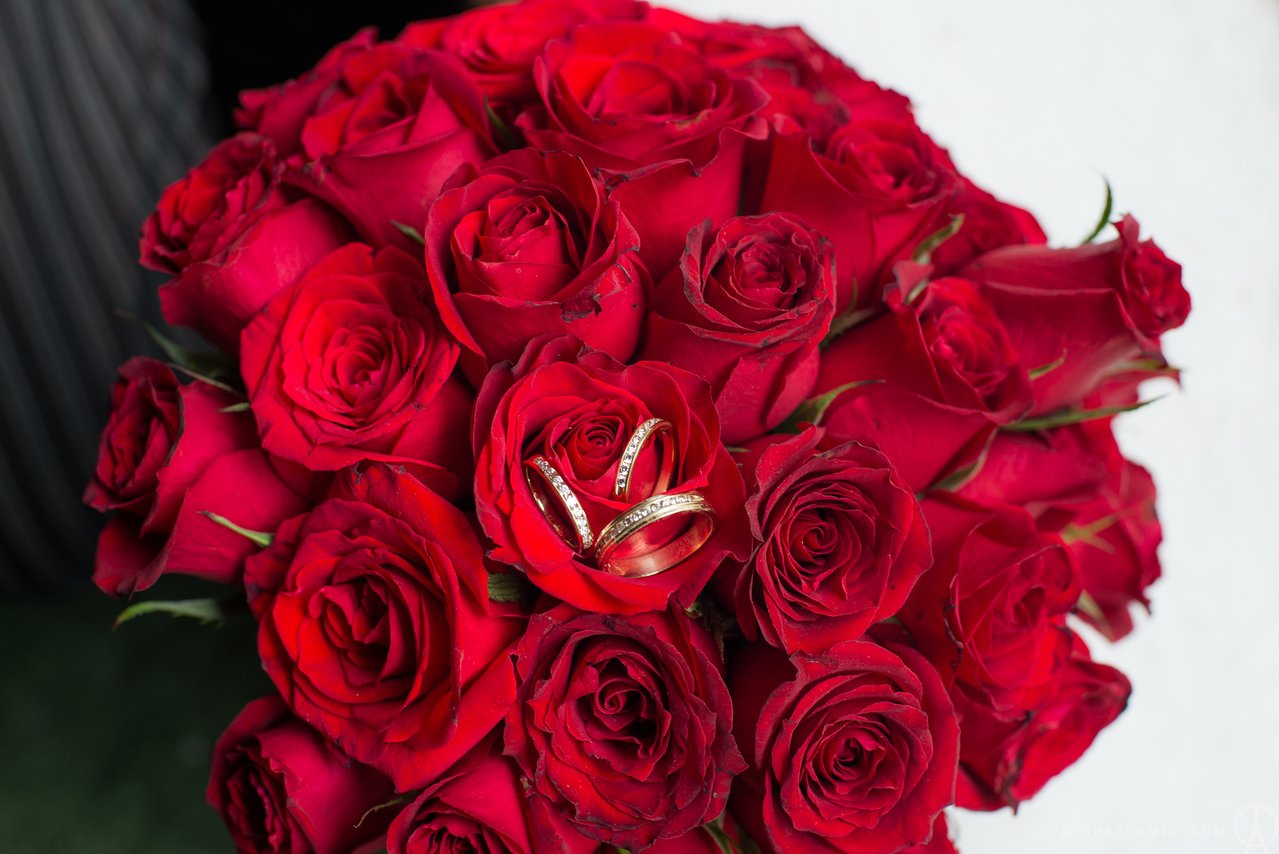 A bouquet of red roses with wedding rings placed on one of the roses.