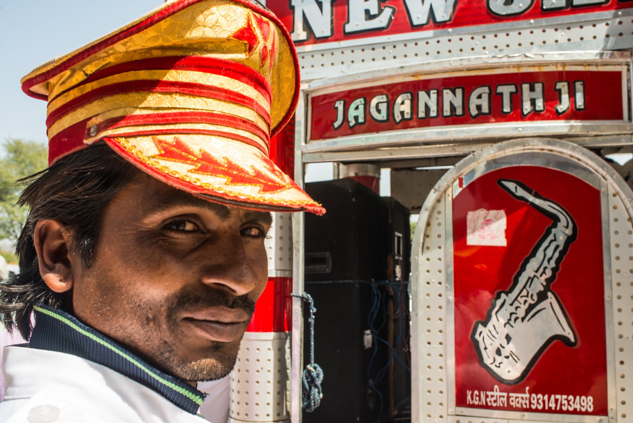 A man wearing a red and yellow hat smiling, standing next to a food cart with a red and white sign and a graphic of a sandwich.