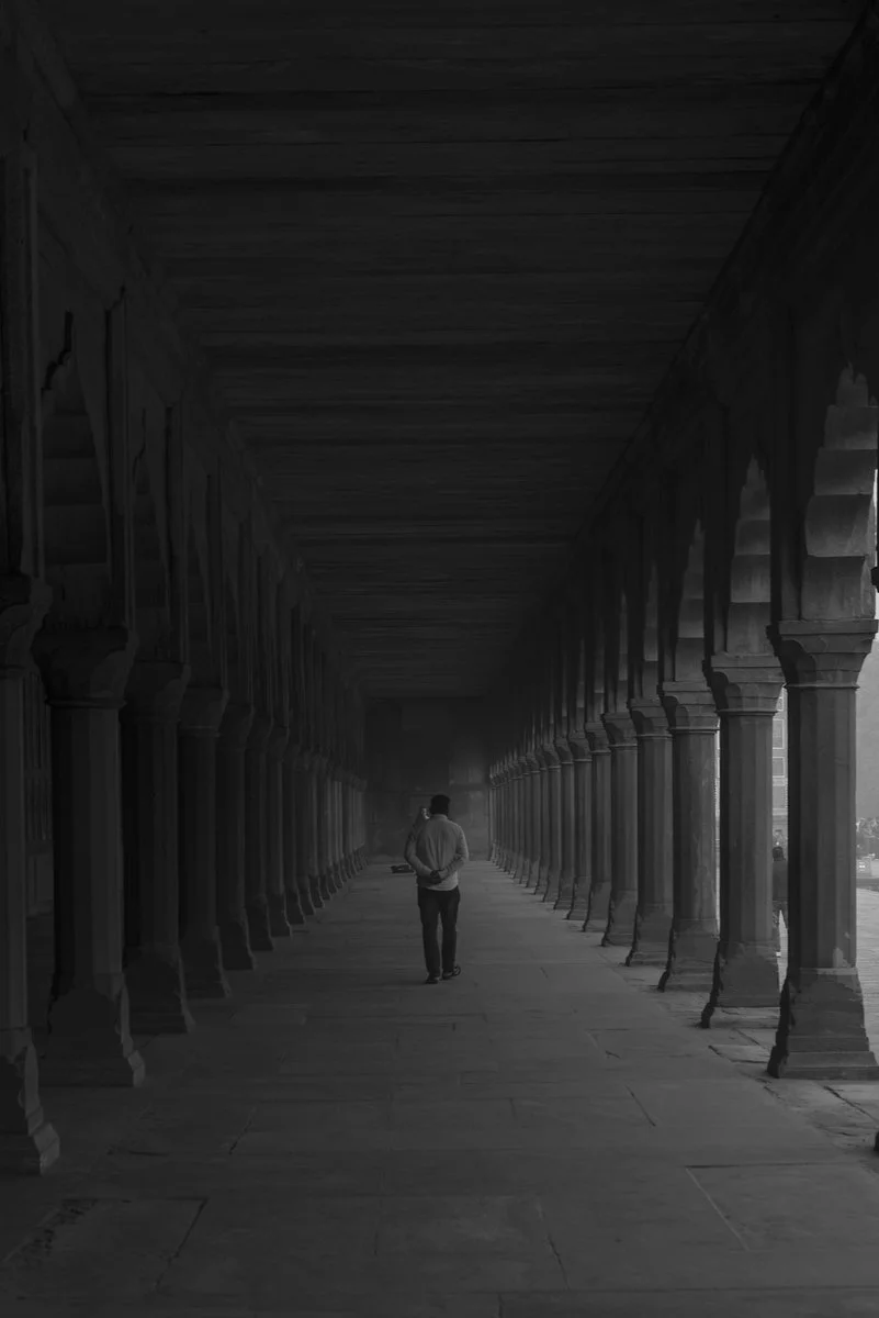 A person walking alone through a long, covered, historic corridor with stone pillars on either side.