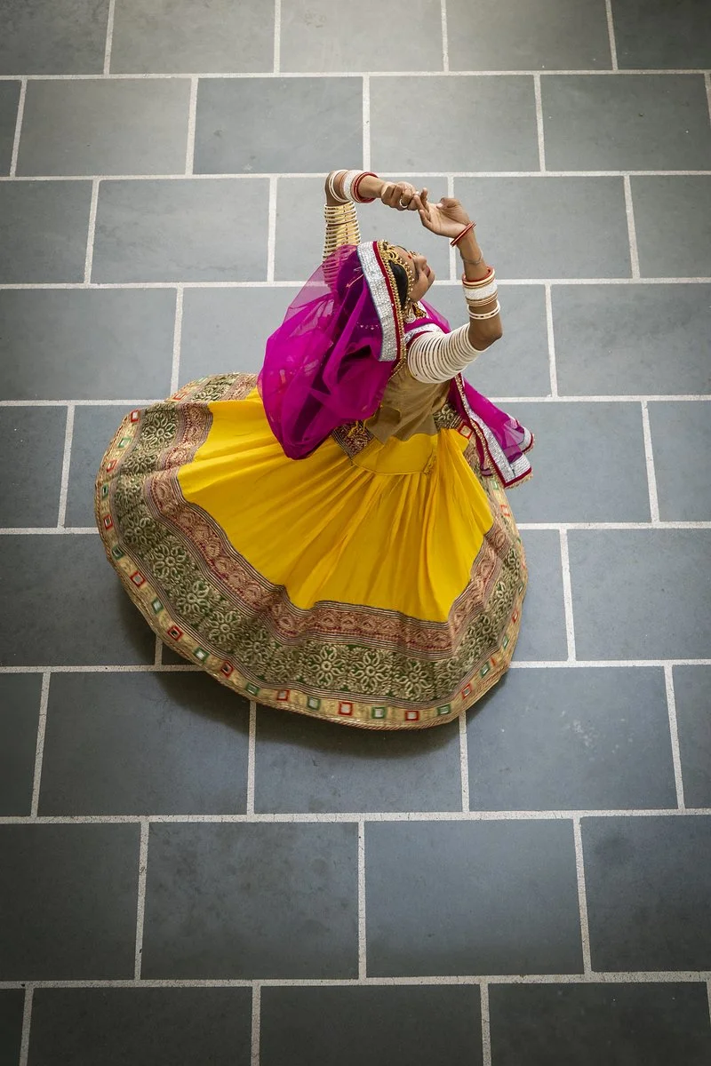 A woman dressed in traditional Indian attire performing a dance on a tiled floor, viewed from above.
