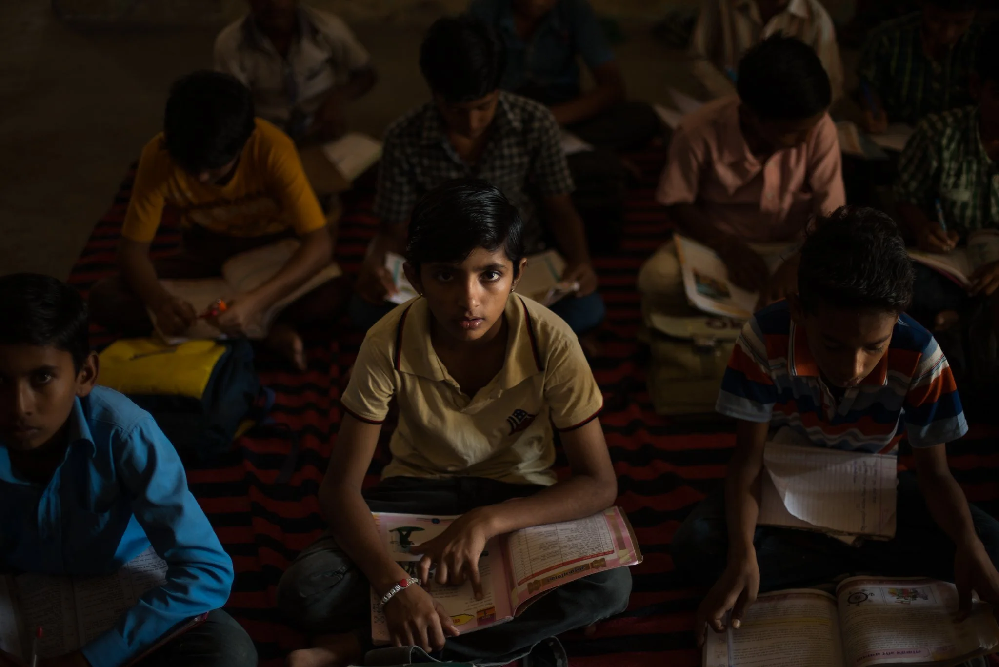 Children sitting on the floor in a dark room, reading textbooks.