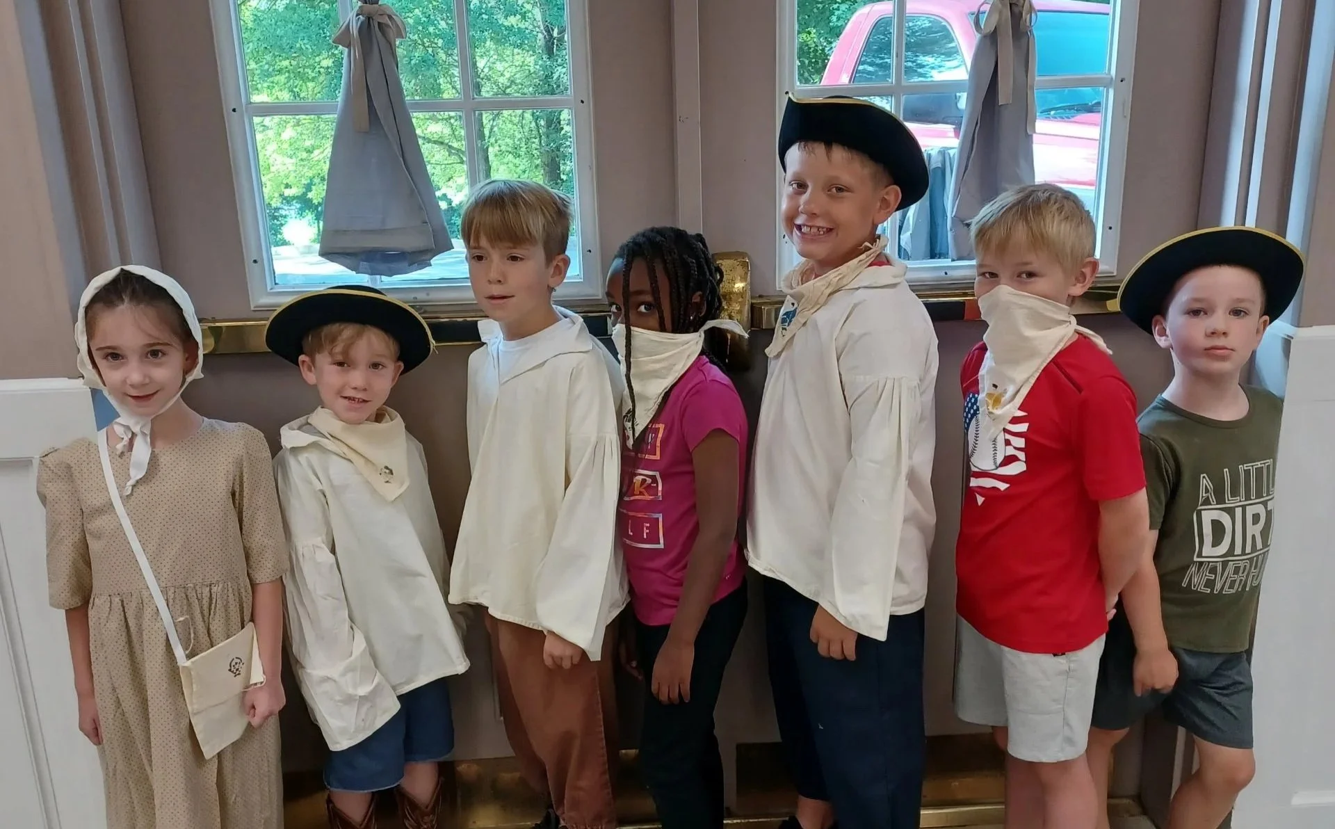 group of campers dressed in colonial hats and tunics smile for a photo at camp