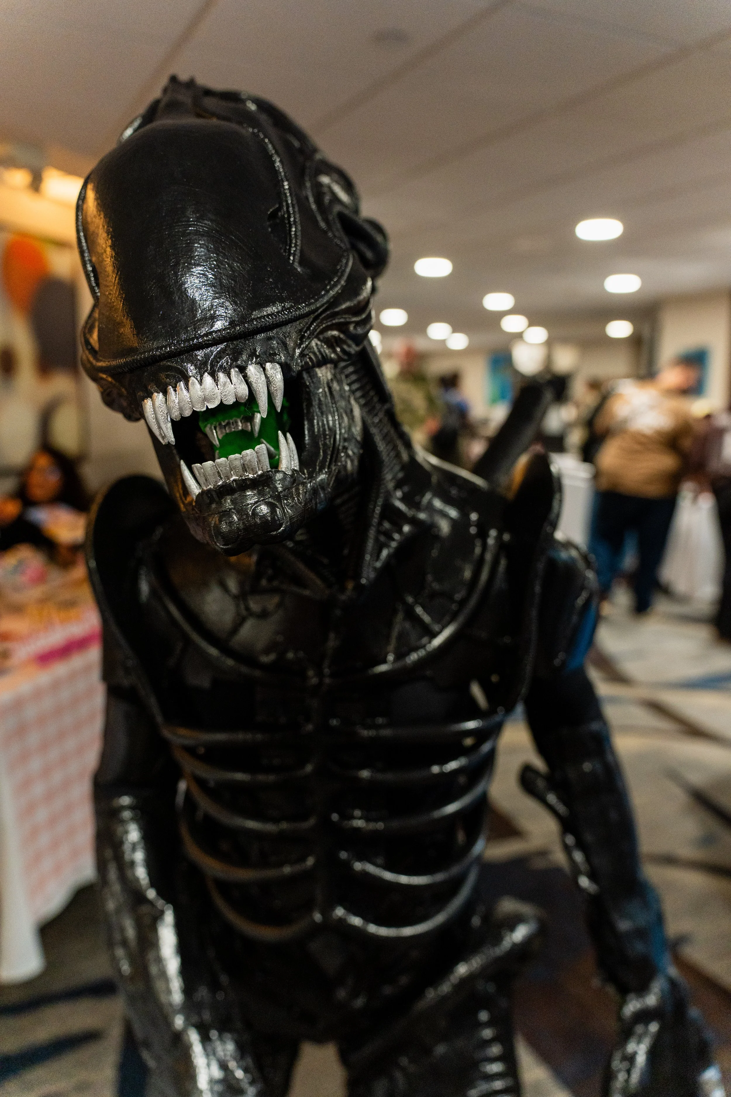 A life-sized replica of the alien from 'Alien', featuring a black, glossy exoskeleton and a detailed skull with sharp teeth, set in a crowded indoor space.
