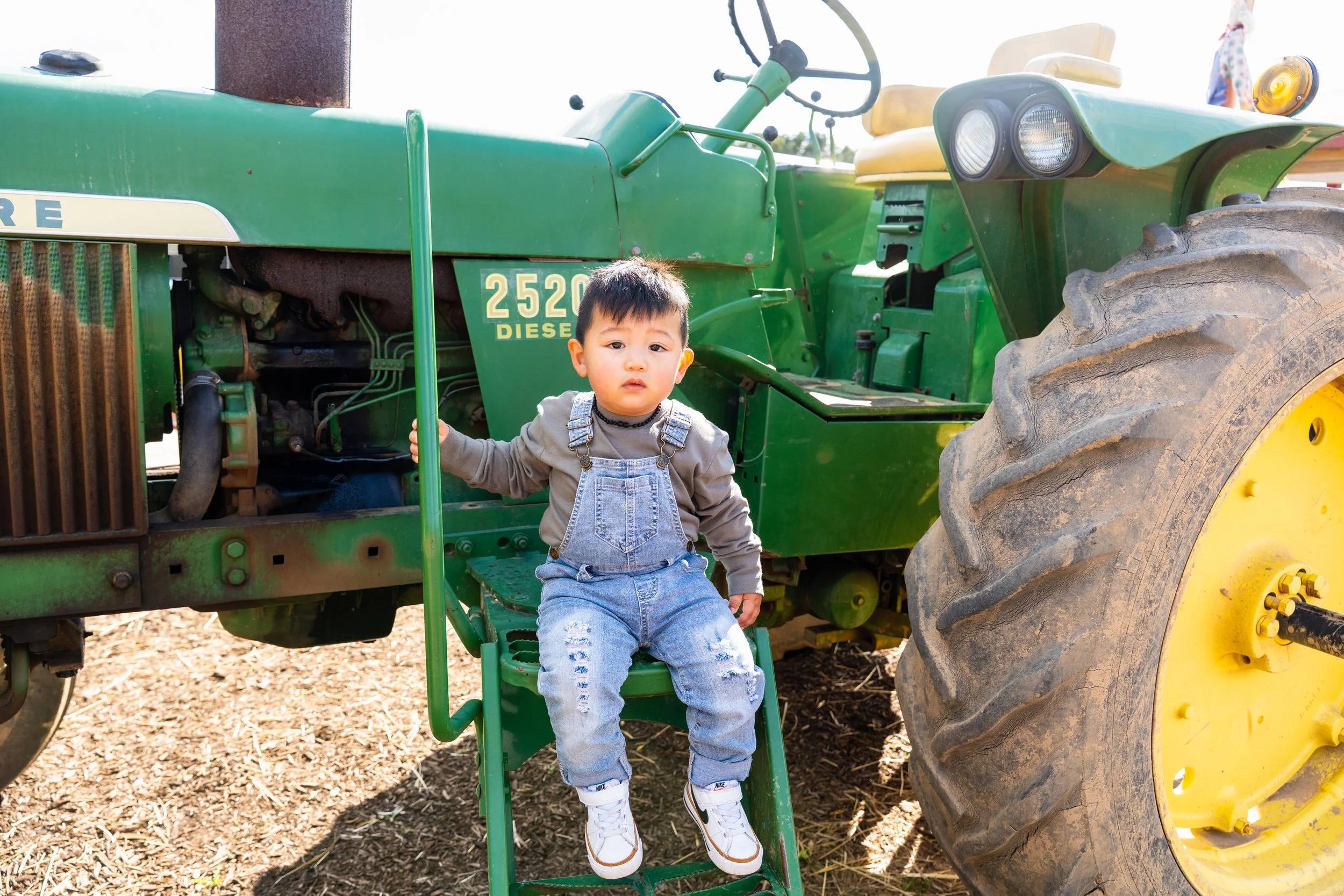 A young boy sitting on a small green step ladder in front of a large green tractor.