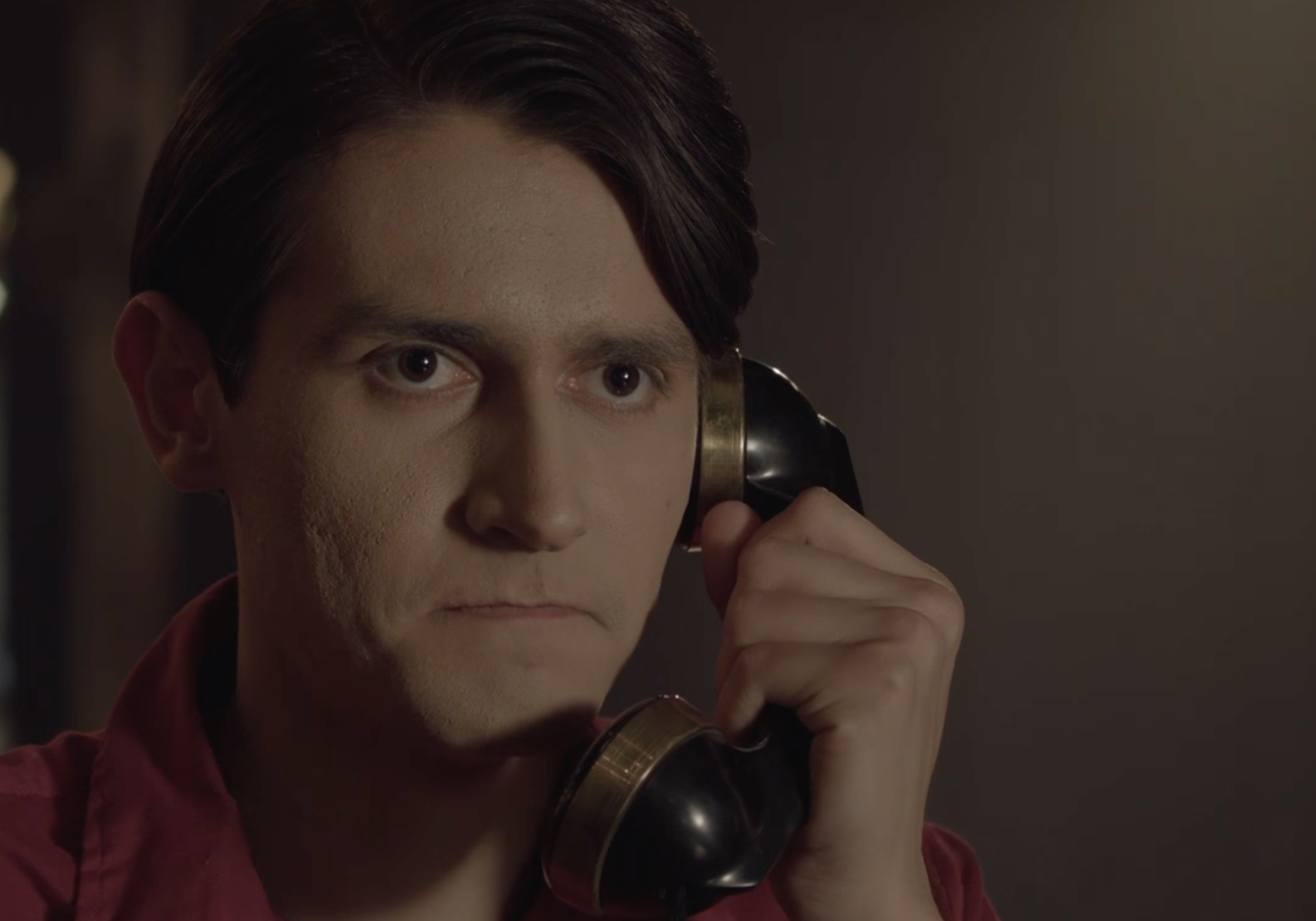 Gavin Velez holding an old-fashioned telephone to his ear, looking intently.
