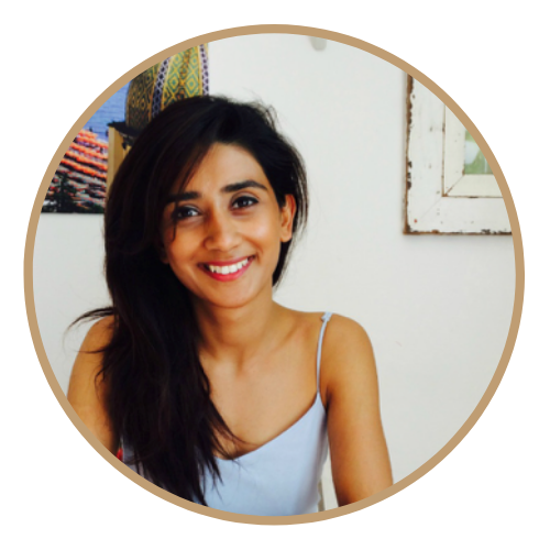 Photo of women called Gursharn Rait smiling with long hair and wearing a blue dress with a pcture on the white wall behind her.