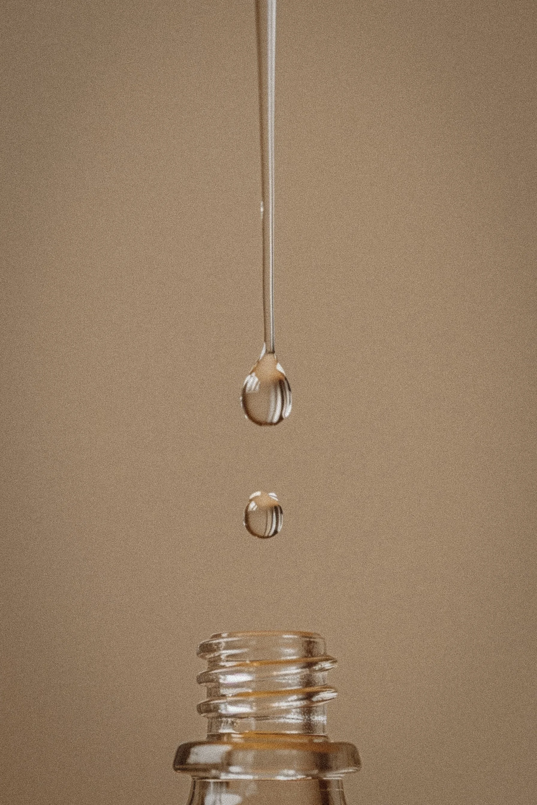 Close-up of a glass dropper with two drops of liquid falling into an open glass bottle.