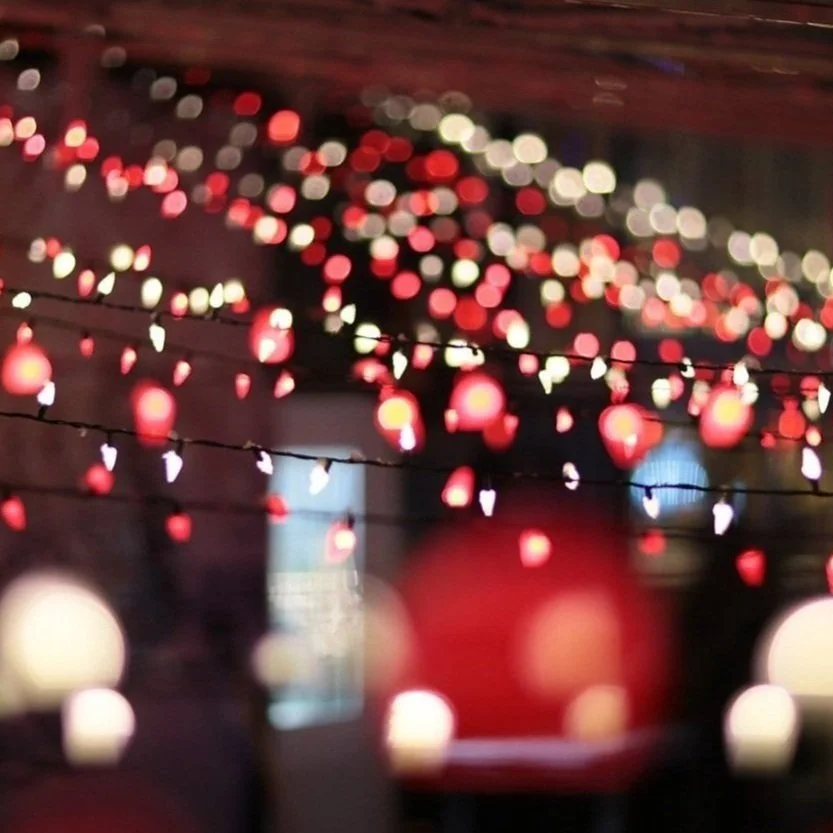 Blurred string lights with red, white, and warm colors hanging in a dark room or outdoor setting, creating a festive or cozy atmosphere.