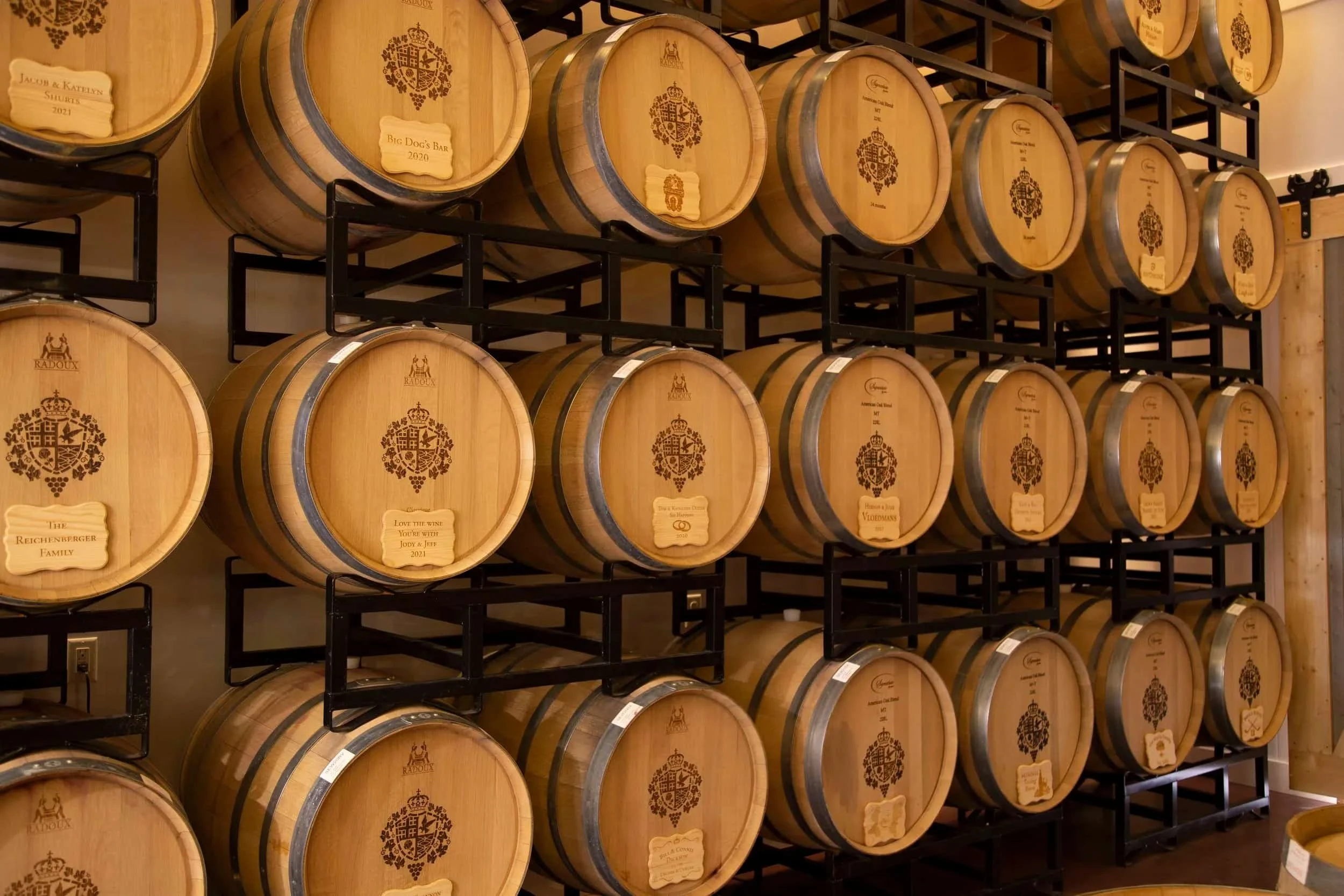 Wine barrels stored on black metal racks in a winery or cellar.