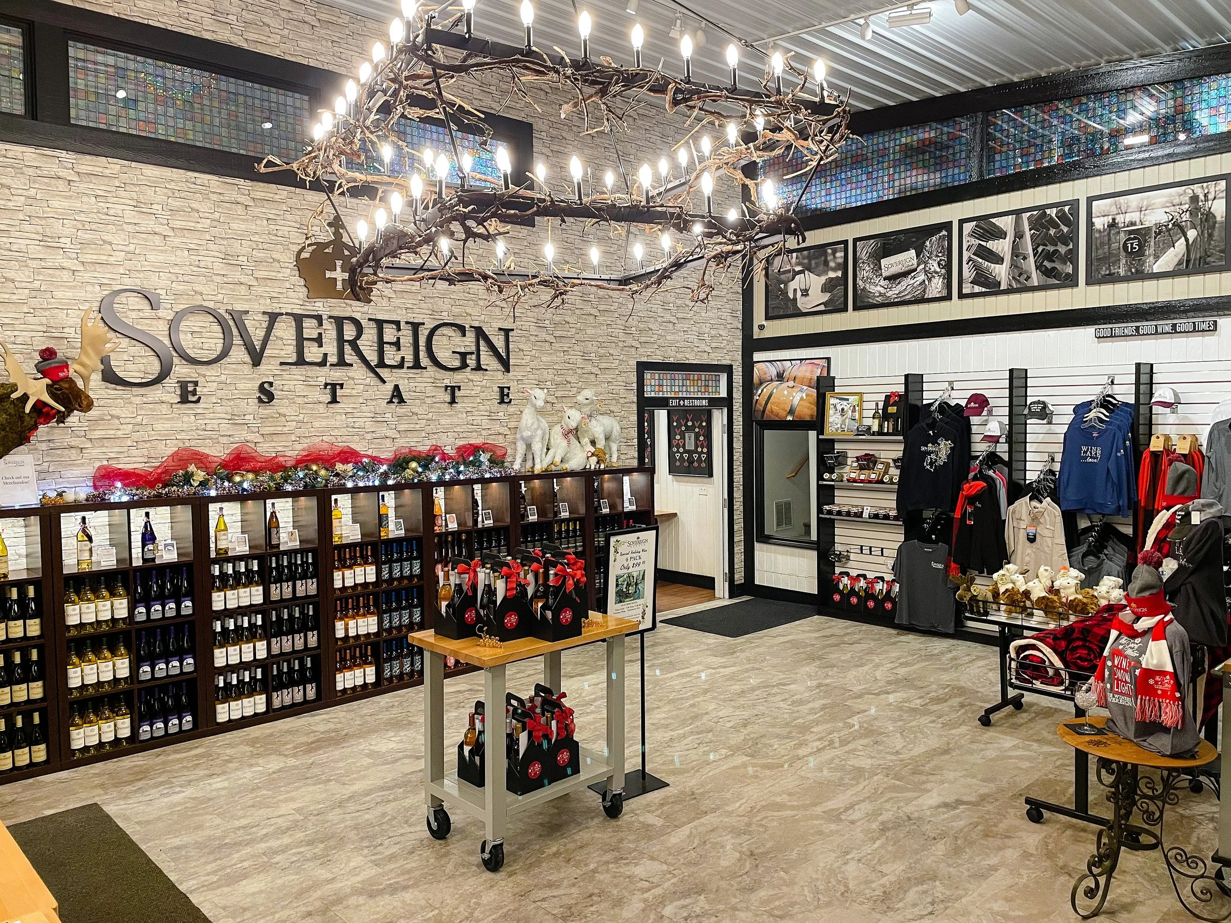 Interior of Sovereign Estate retail store decorated for Christmas with shelves of wine, apparel, and accessories, a large chandelier made of twigs and lights hanging from the ceiling, and festive holiday decorations.