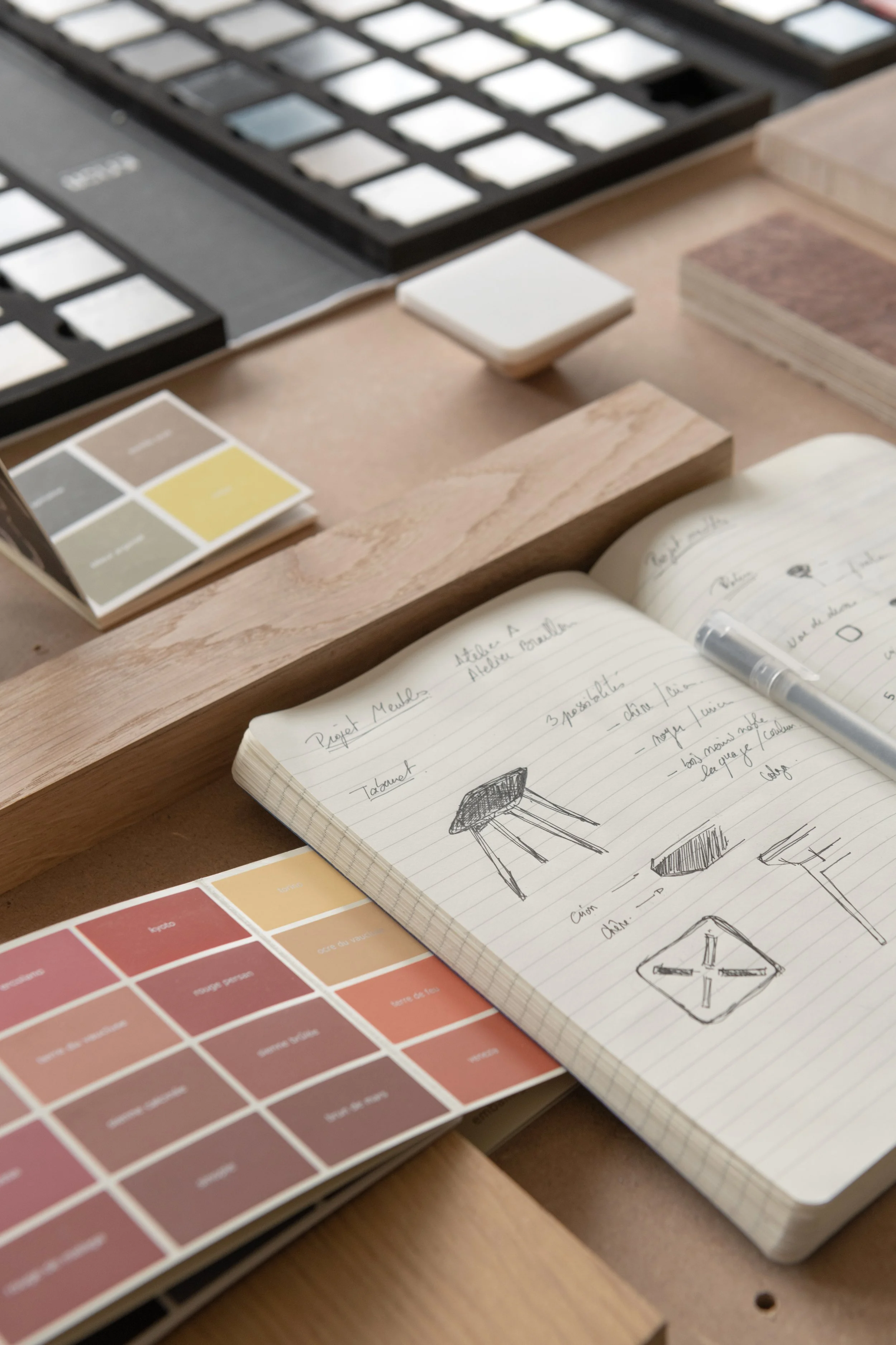 Bloc-notes avec croquis de meubles, échantillons de couleurs et de matériaux sur une table.