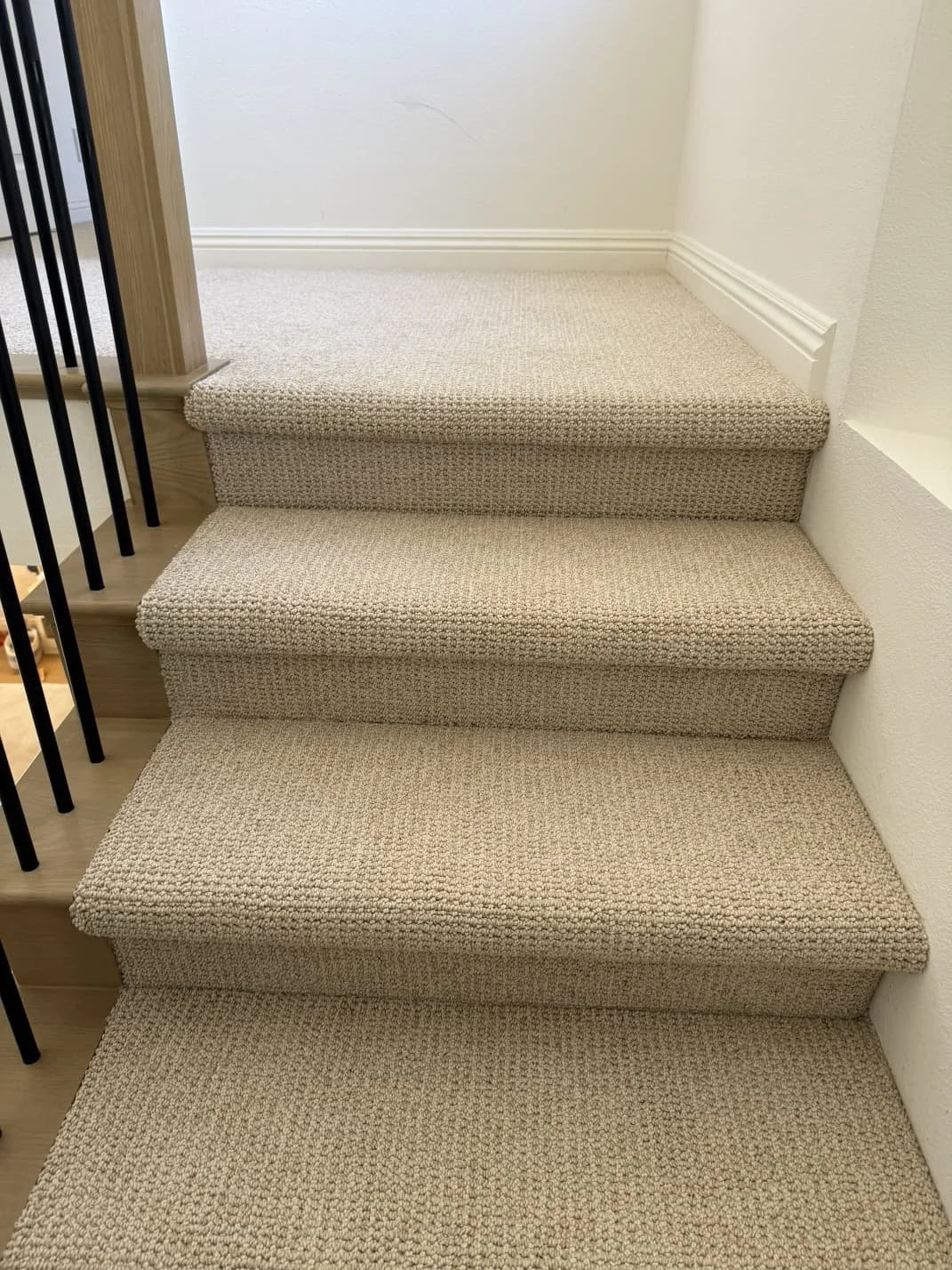 Carpeted staircase with four steps and a white wall on the right side.