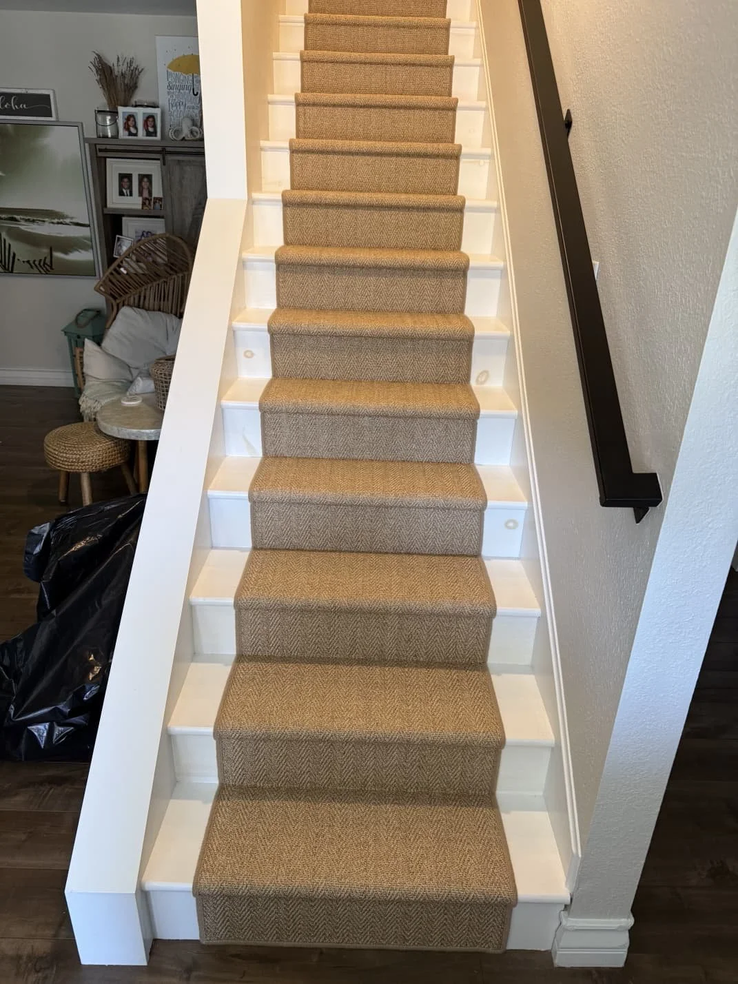 Staircase with beige carpet runner, white risers, and a dark handrail on the right wall in a home interior.