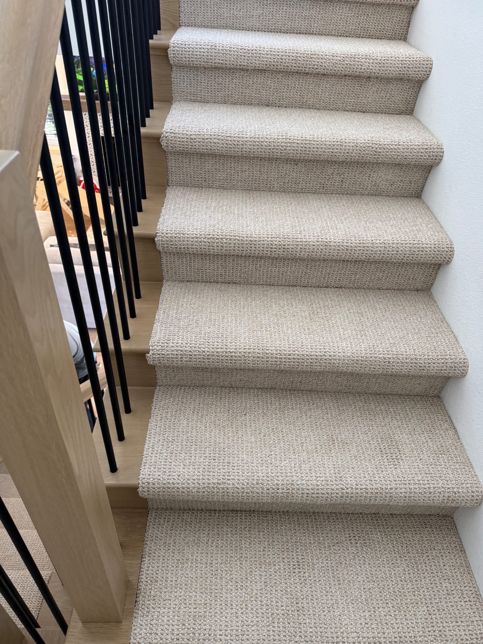 Carpeted staircase with beige carpet and black metal railings on the left side, adjacent to a white wall.