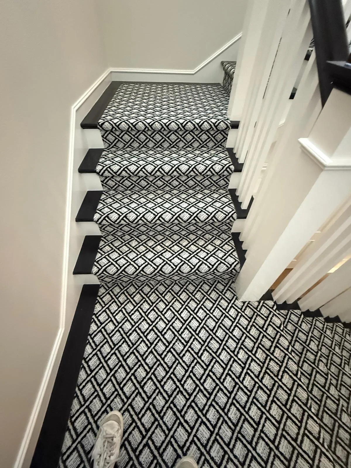 Photo of a staircase with patterned carpet, black risers, and white walls, taken from the top looking down.