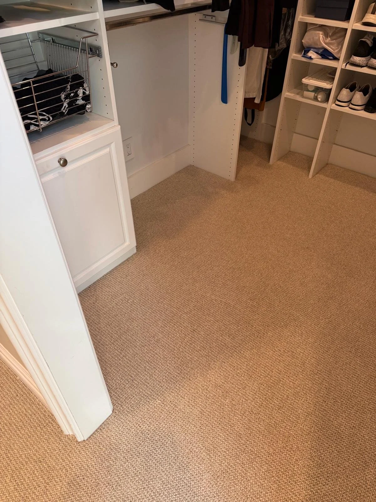 An empty walk-in closet with shelves and hangers, some shoes, and folded clothes on the shelves.