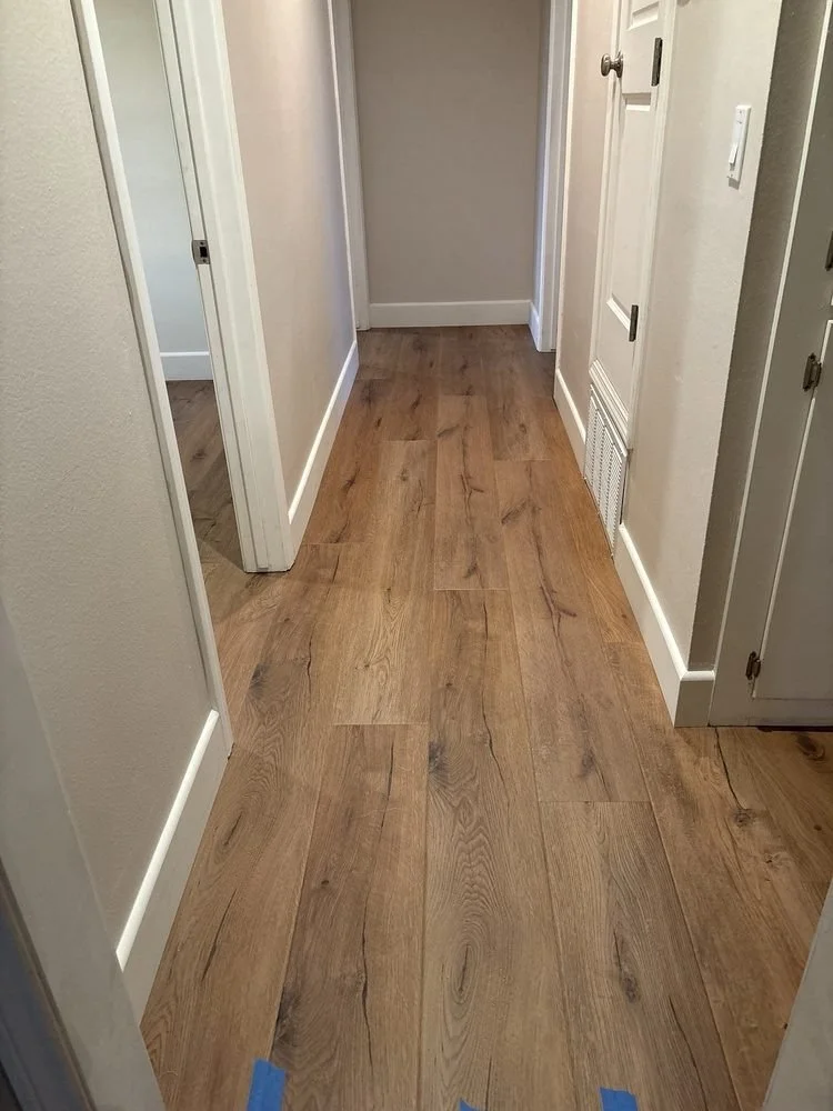 A hallway with wooden flooring, white walls, and white baseboards. There are doorways on the left and right sides and a closed door at the end of the hall.