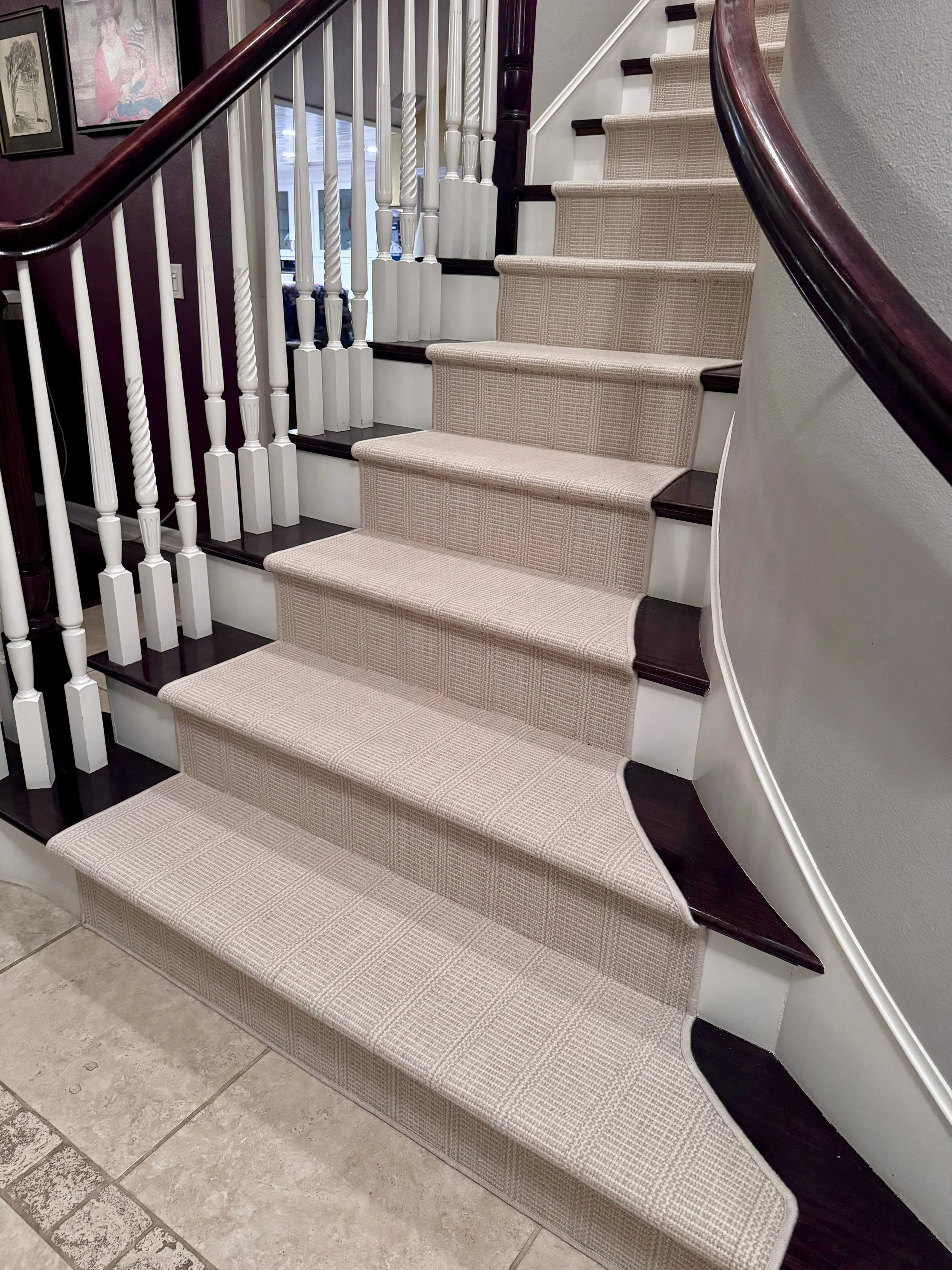 Staircase with beige carpet runner, dark wood steps, white balusters, and curved dark wood handrail.