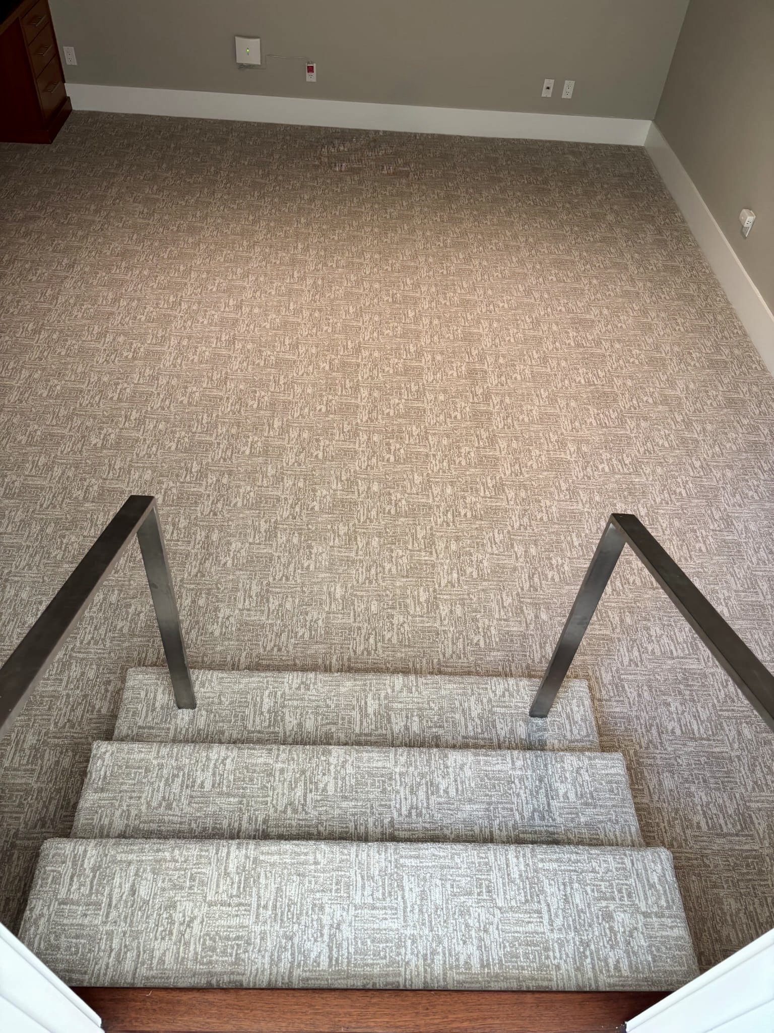 Empty carpeted staircase viewed from above with metal handrails on either side in an indoor setting.