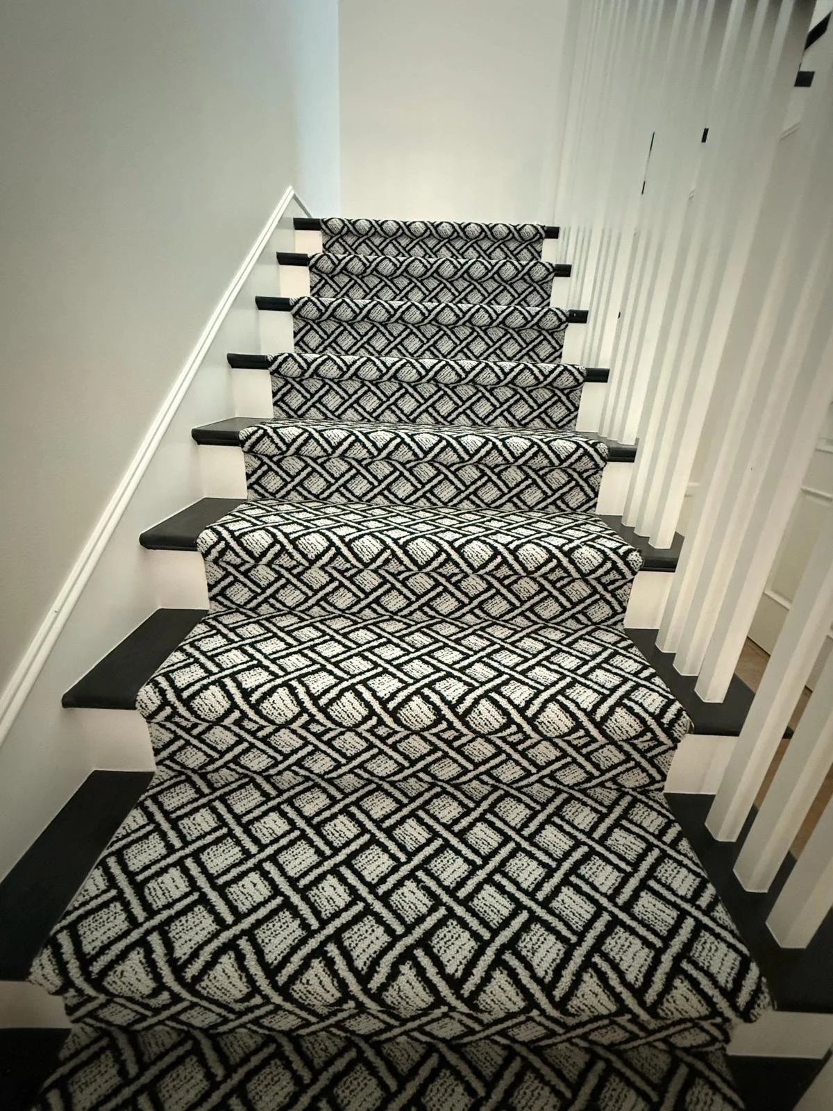 Black and white patterned carpeted staircase with black steps and white walls.