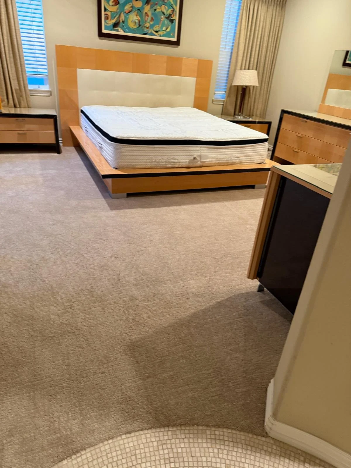 Hotel room with a large bed, nightstands, a dresser, a TV, and a window with blinds and beige curtains.