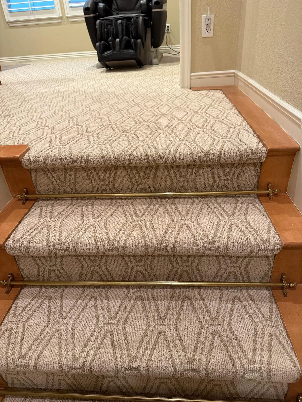 Carpeted staircase with three steps, brass handrails on each side, wood trim, and a massage chair in the background near a wall outlet.