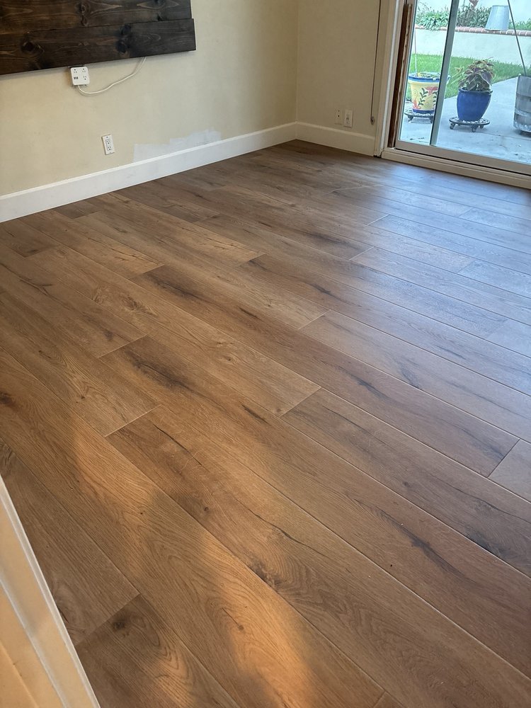 Room with light brown wood flooring and sliding glass door leading outside to a patio with potted plants.