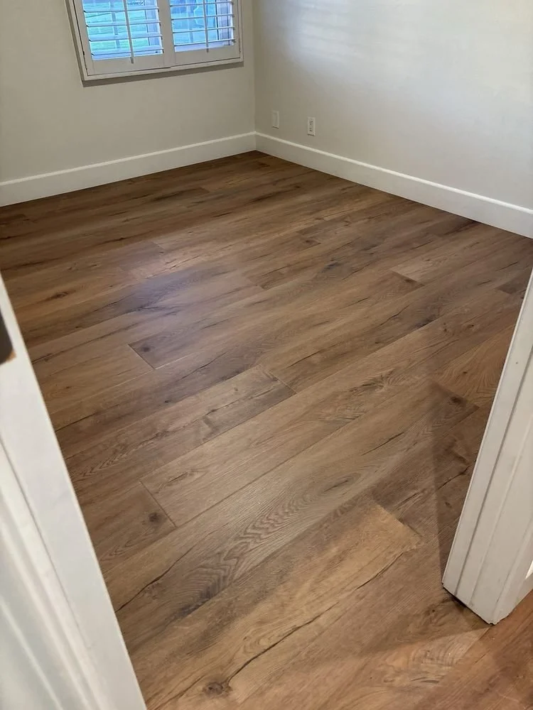 Empty room with hardwood flooring, white walls, white baseboards, and a window with blinds.