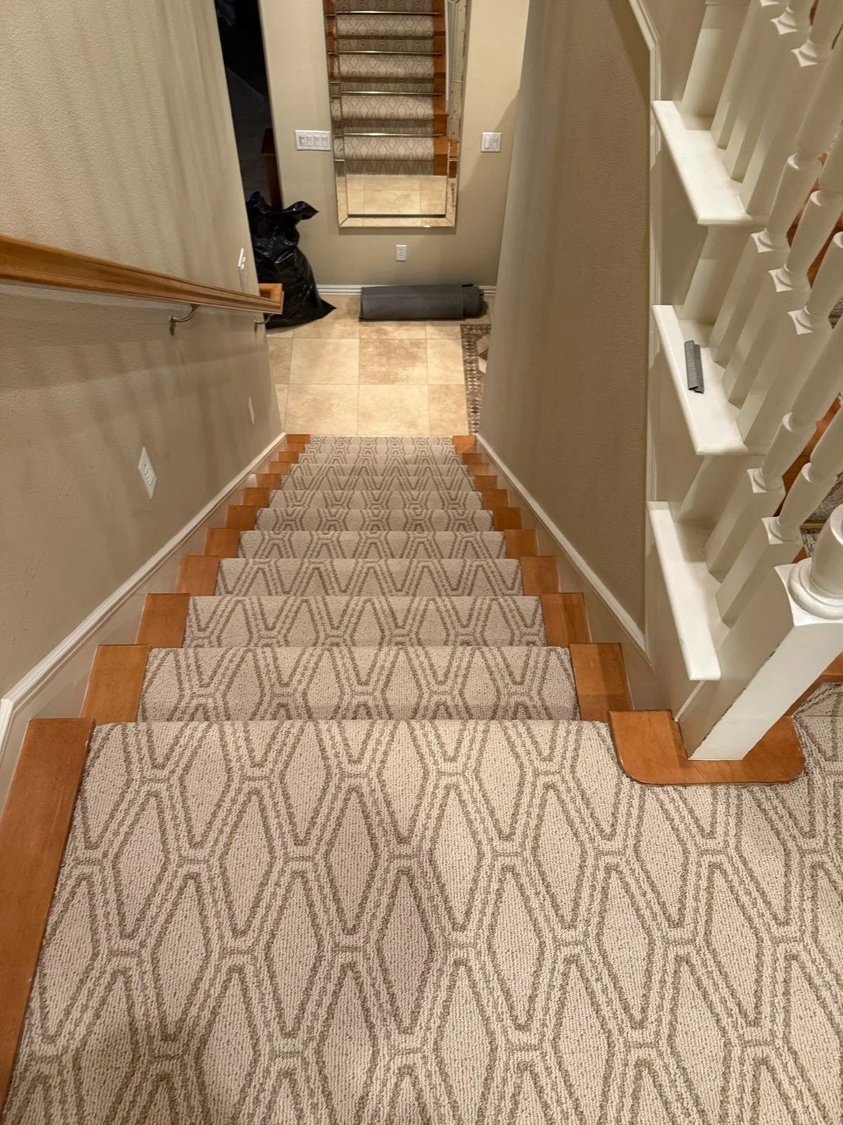 Top of carpeted staircase looking down into a tiled entryway with stairs leading up and another flight visible ahead.