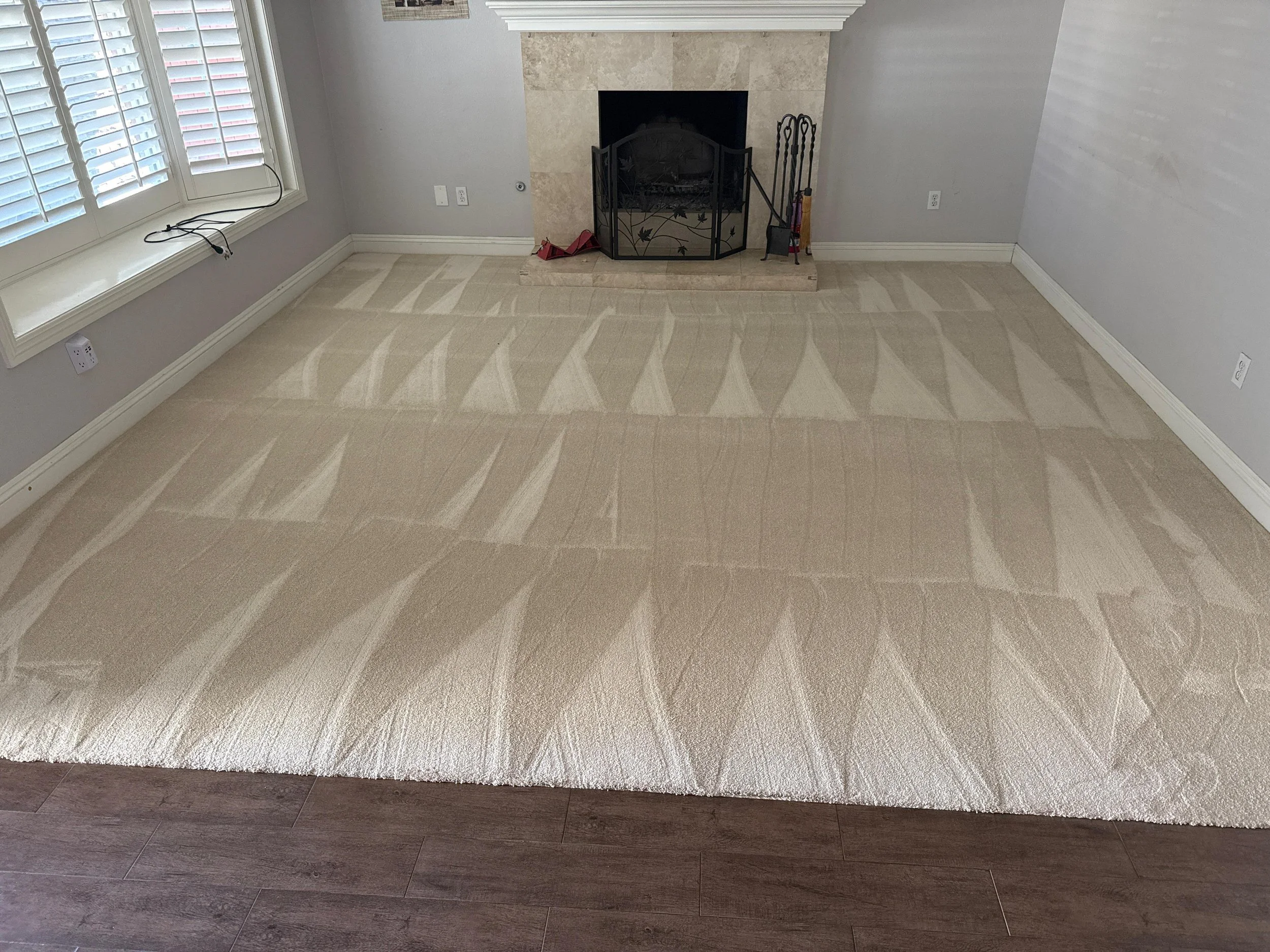 Empty living room with beige carpet, fireplace, and large window with blinds.