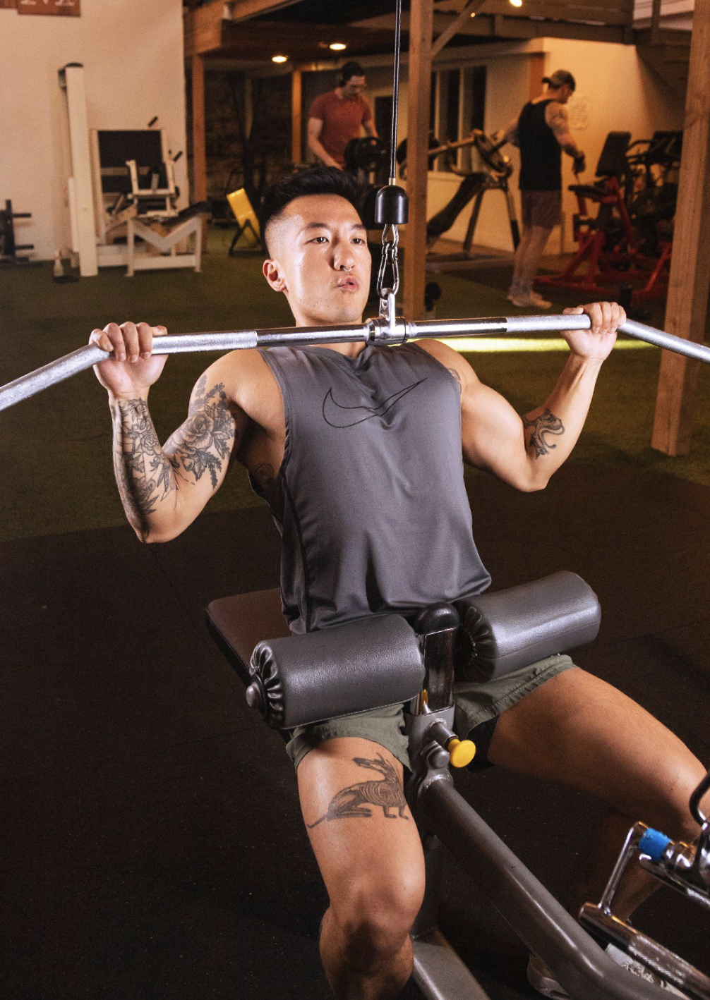 Lifter using a lat pulldown machine while other gymgoers work out in the background, an example of staying in your own bubble at a busy gym.