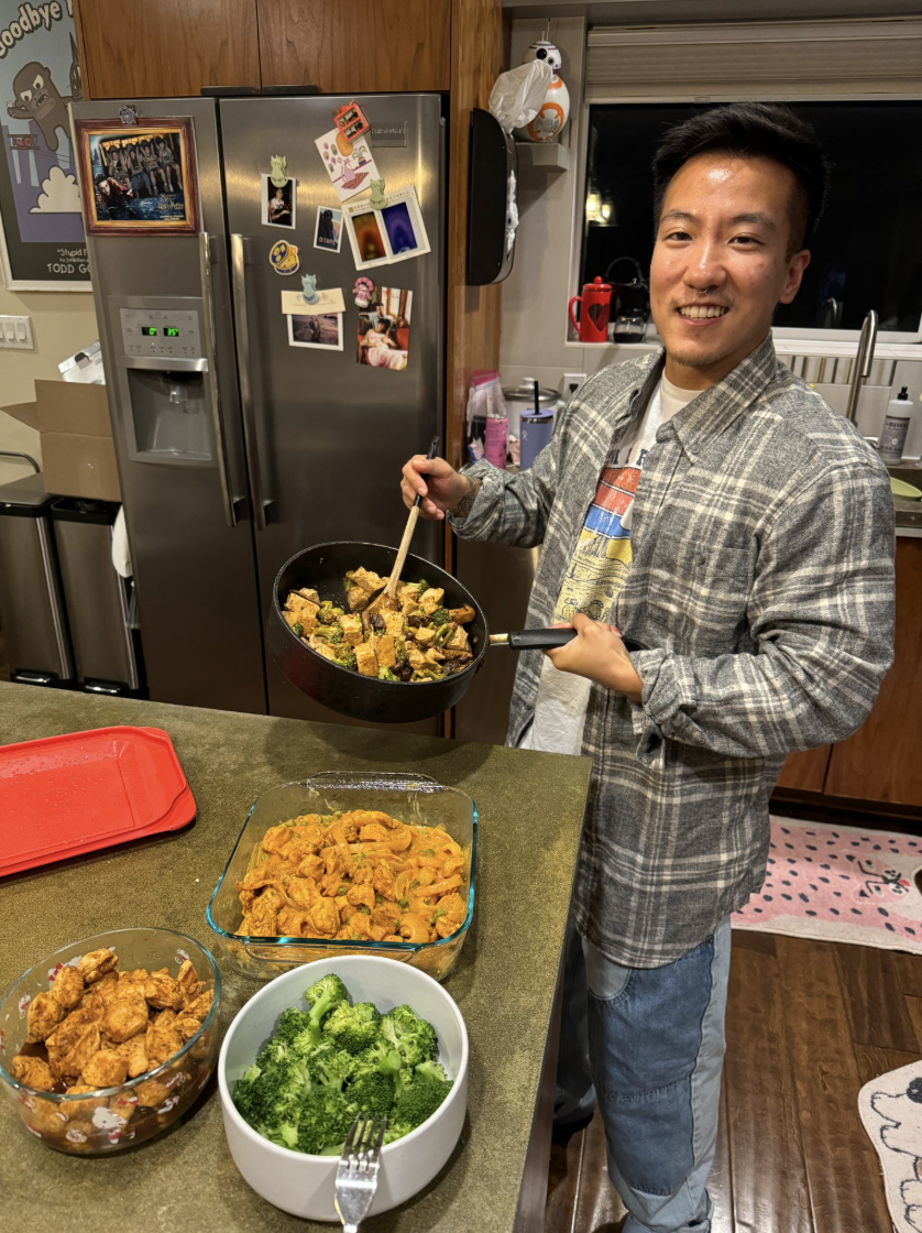 Landyn Pan smiling while cooking a skillet meal at home, with bowls of roasted sweet potatoes and broccoli on the counter