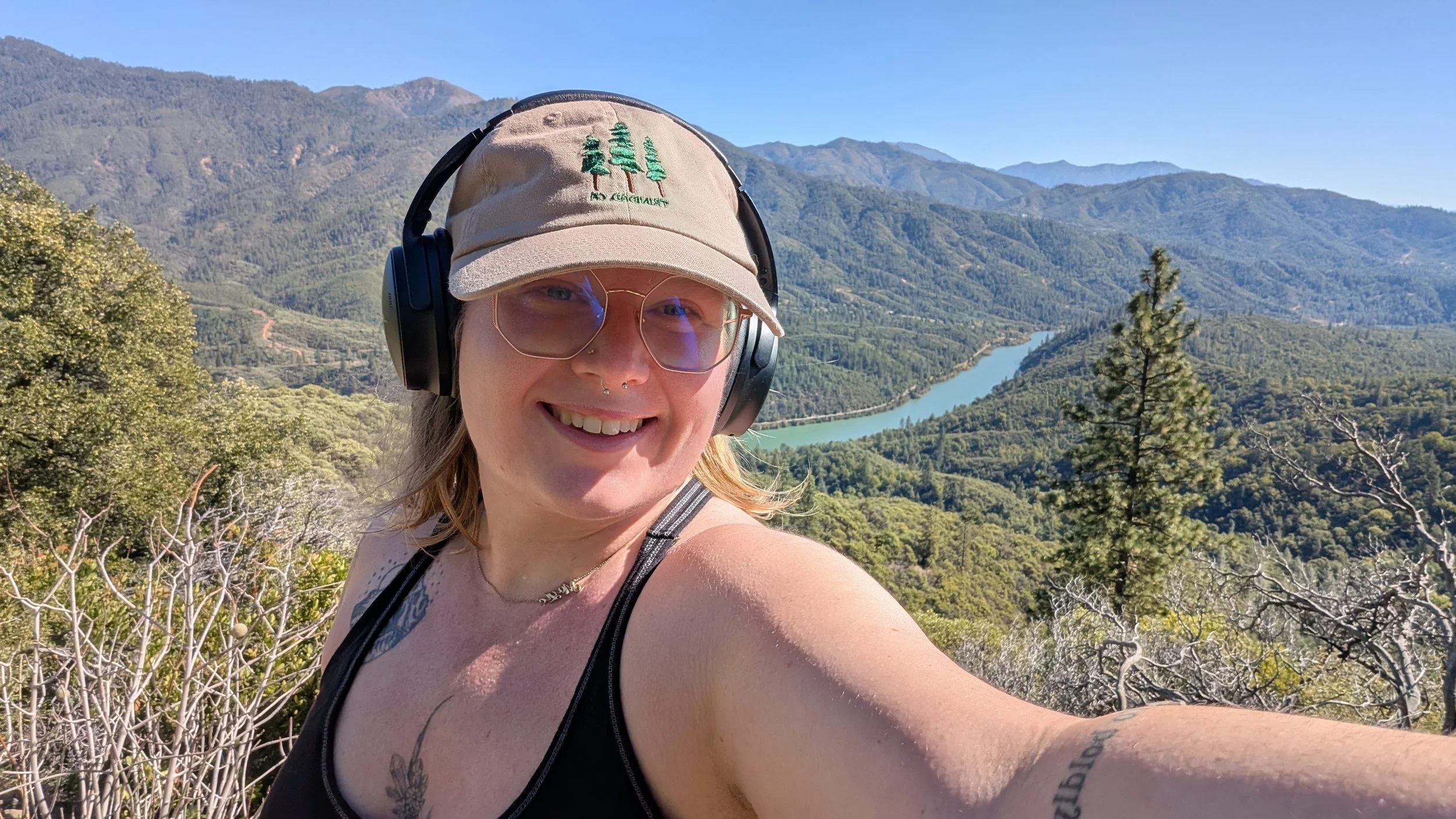 A woman smiling with mountains, a lake, and trees in the background.